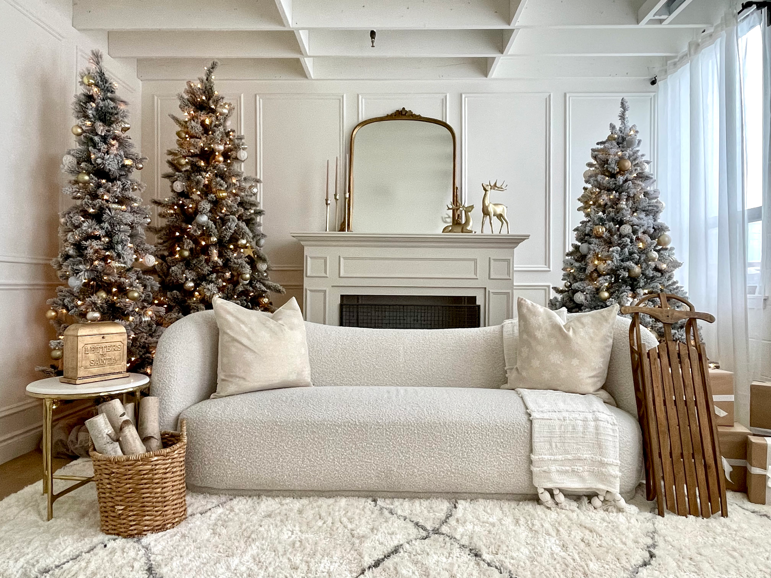 Minimalist modern living room with white sofa, mirror above fireplace, and three lit Christmas trees decked in warm lights.