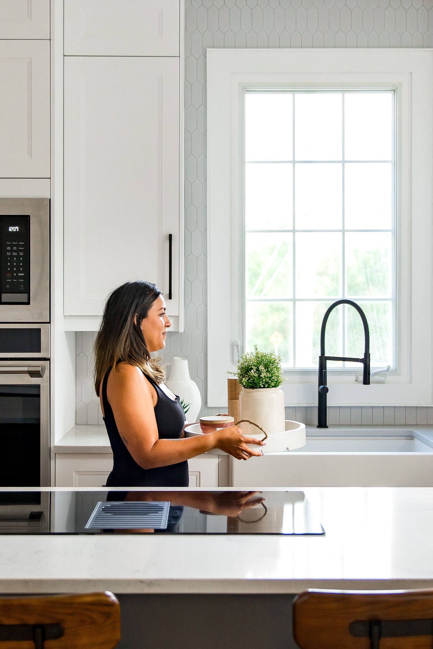 Interior designer in modern white kitchen interior with a black faucet, built-in appliances, and natural light streaming through the window.