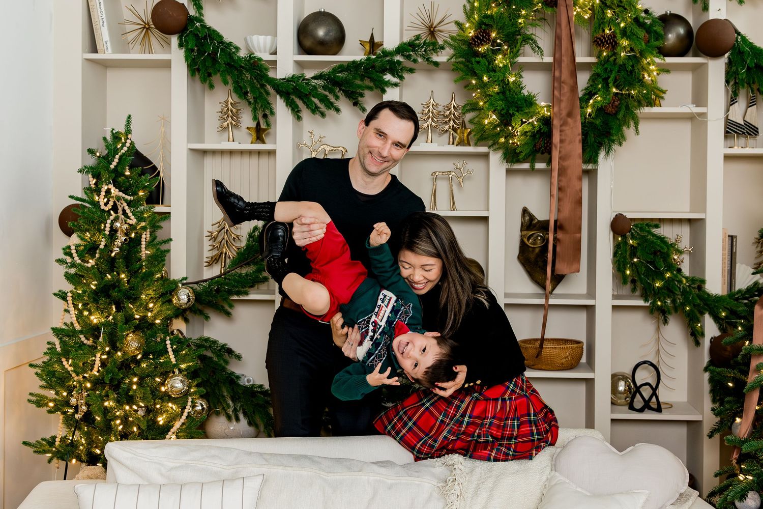 A festive holiday scene with people sitting on a white bench surrounded by Christmas decorations and greenery.