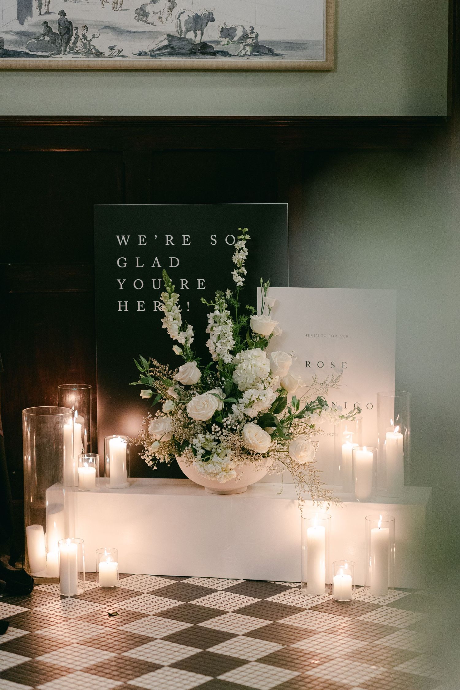 Elegant wedding welcome display with white floral arrangement, glowing candles and a checkered floor at the Hotel du Village in New Hope, PA