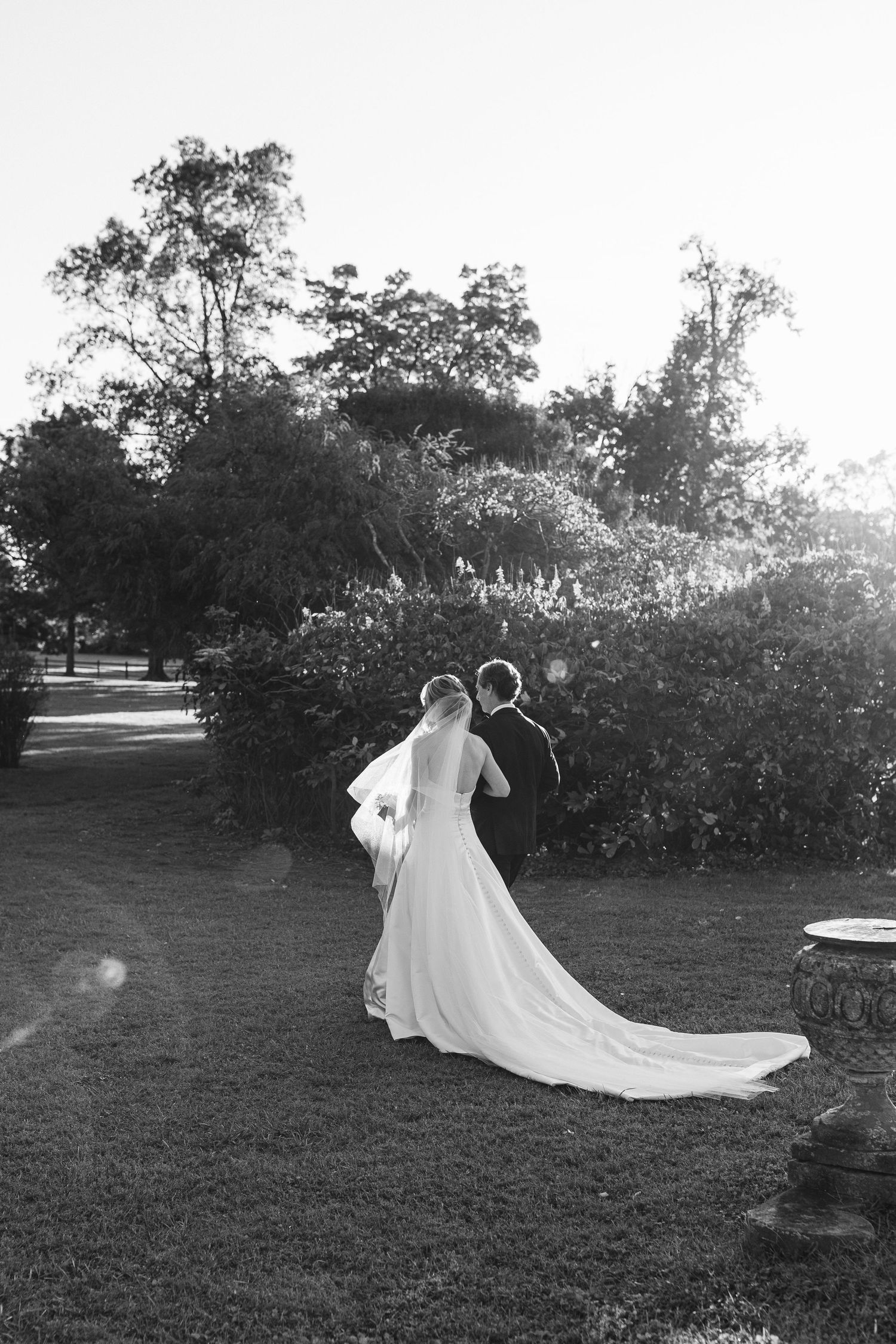 Long train of a wedding dress sweeps across green grass in afternoon light.