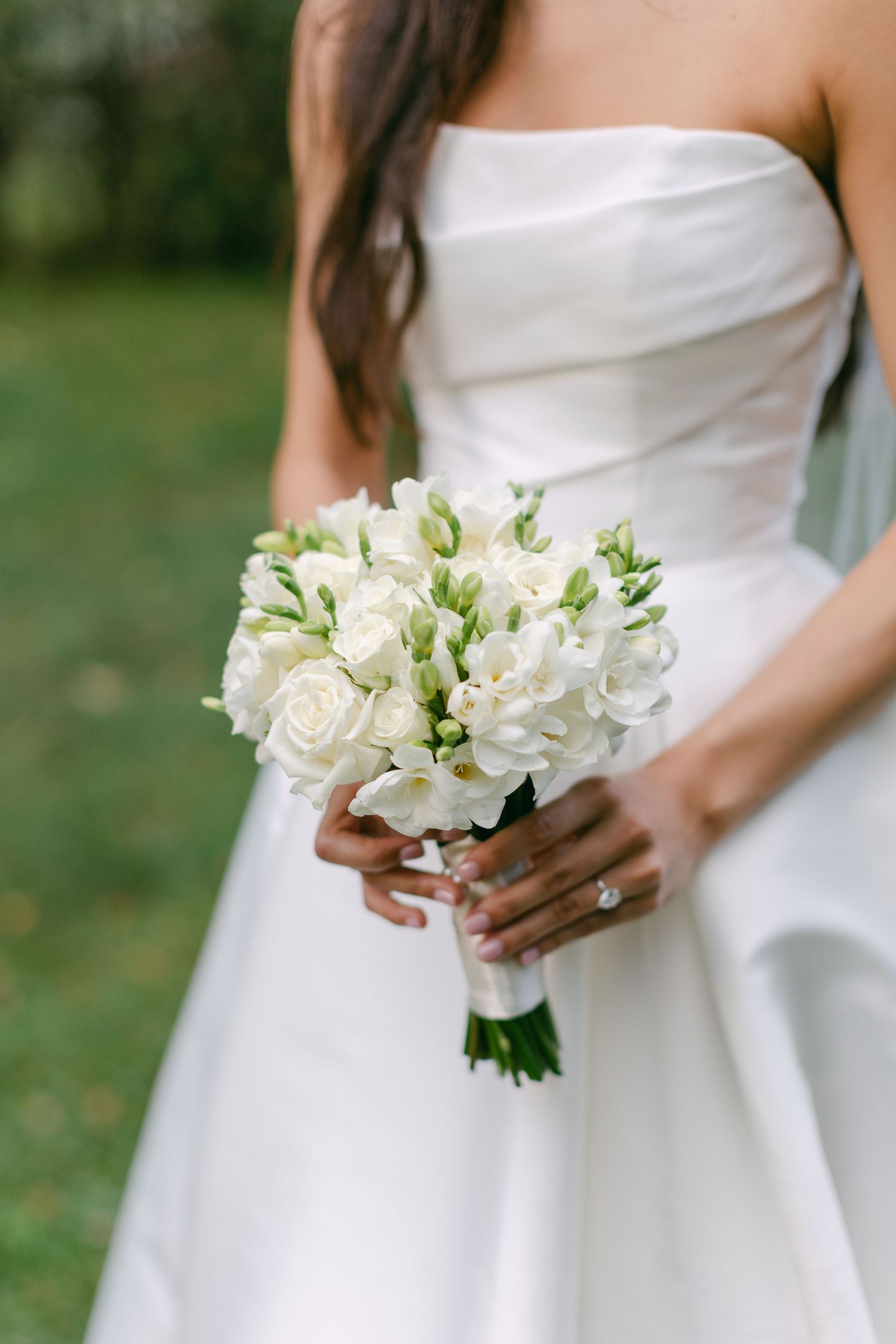 Elegant white bridal bouquet of roses and flowers held against a classic white wedding gown.