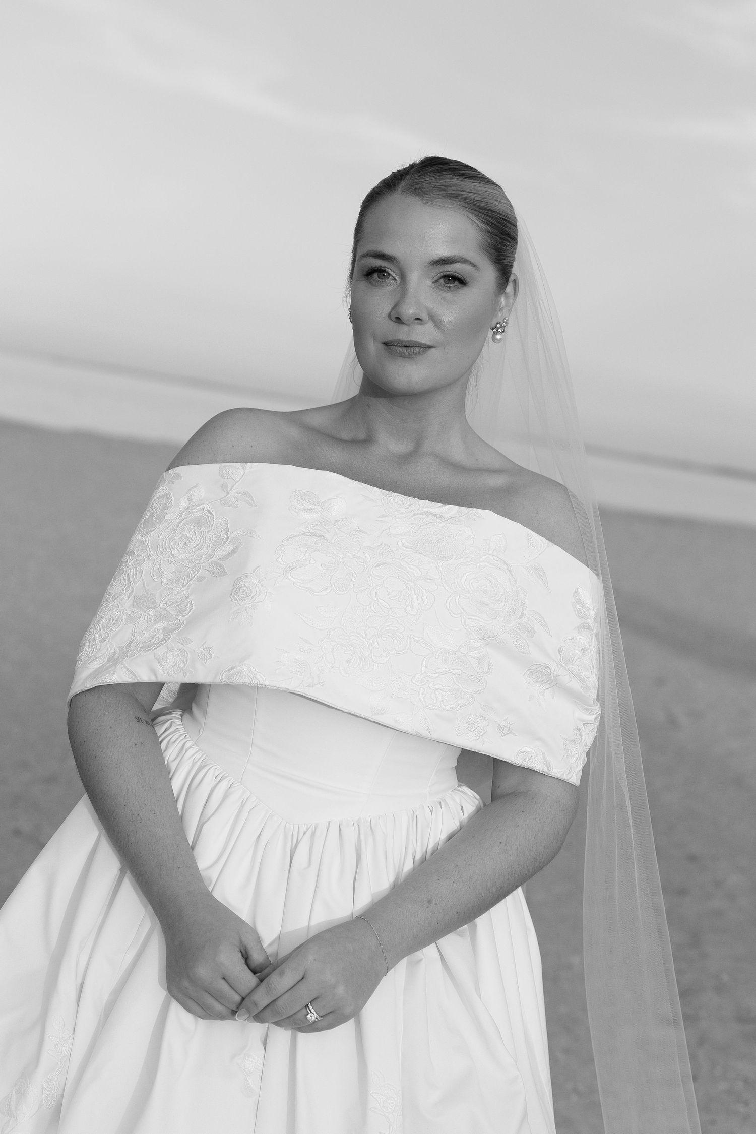 A bride in an elegant off-shoulder white wedding dress poses for a vogue style coastal photographs by a philadelphia wedding photographer.