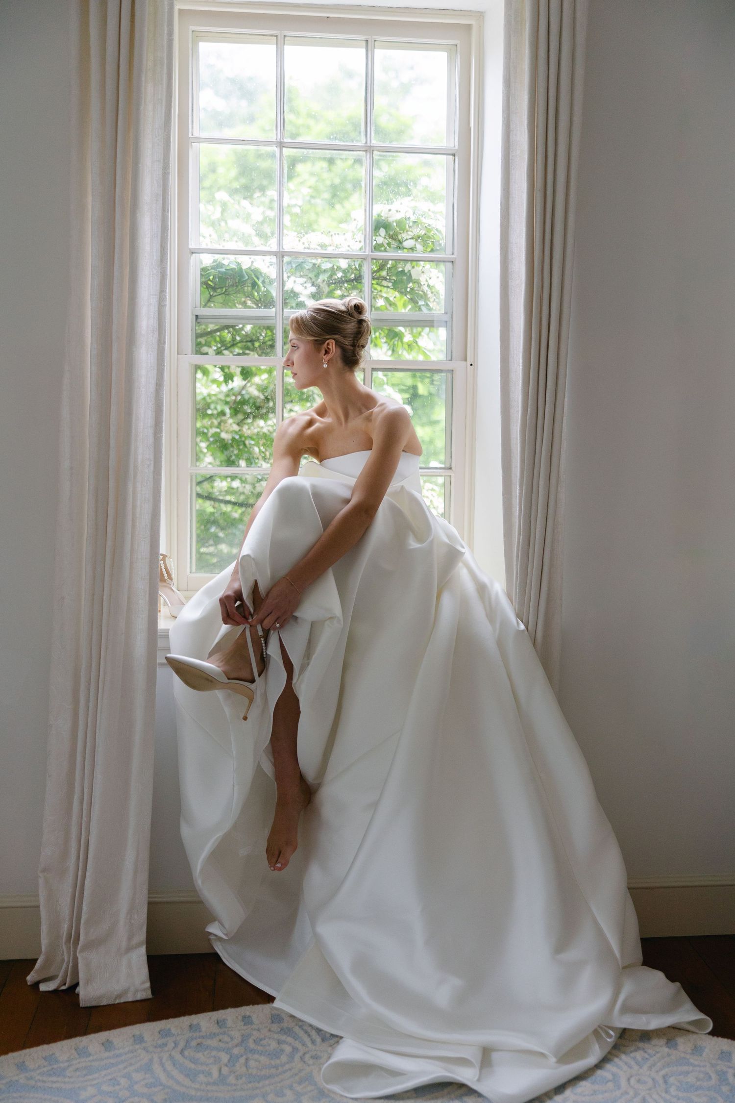 Bride in a flowing white wedding gown sitting on a window sill by a bright window. Philadelphia wedding photographer, timeless elegant bride