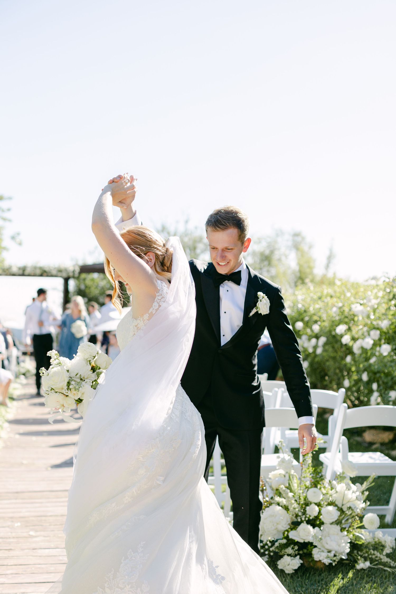 A couple dances together at an outdoor wedding venue surrounded by white floral arrangements.