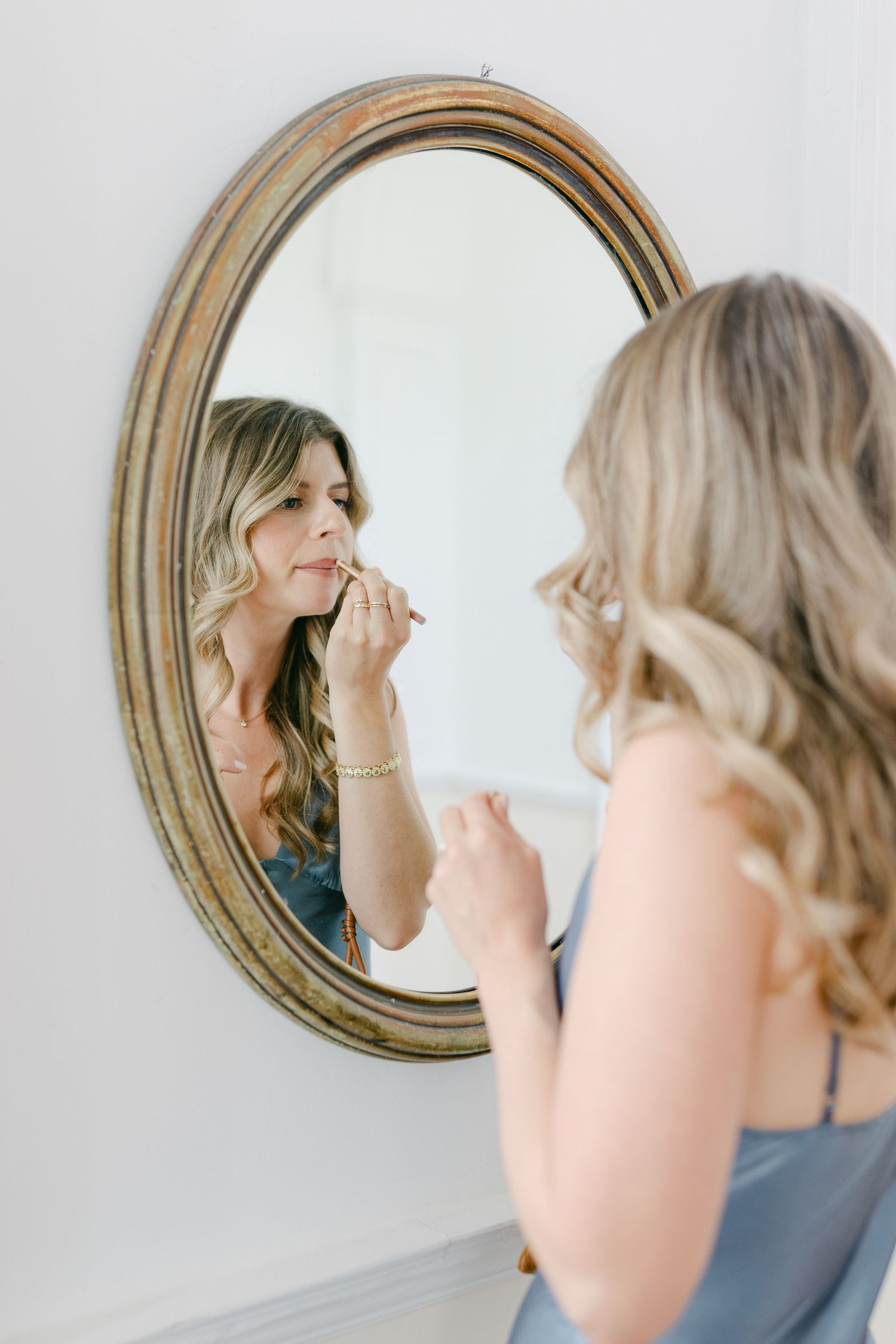 Multiple mirror reflections show wedding day makeup preparation in soft natural light.