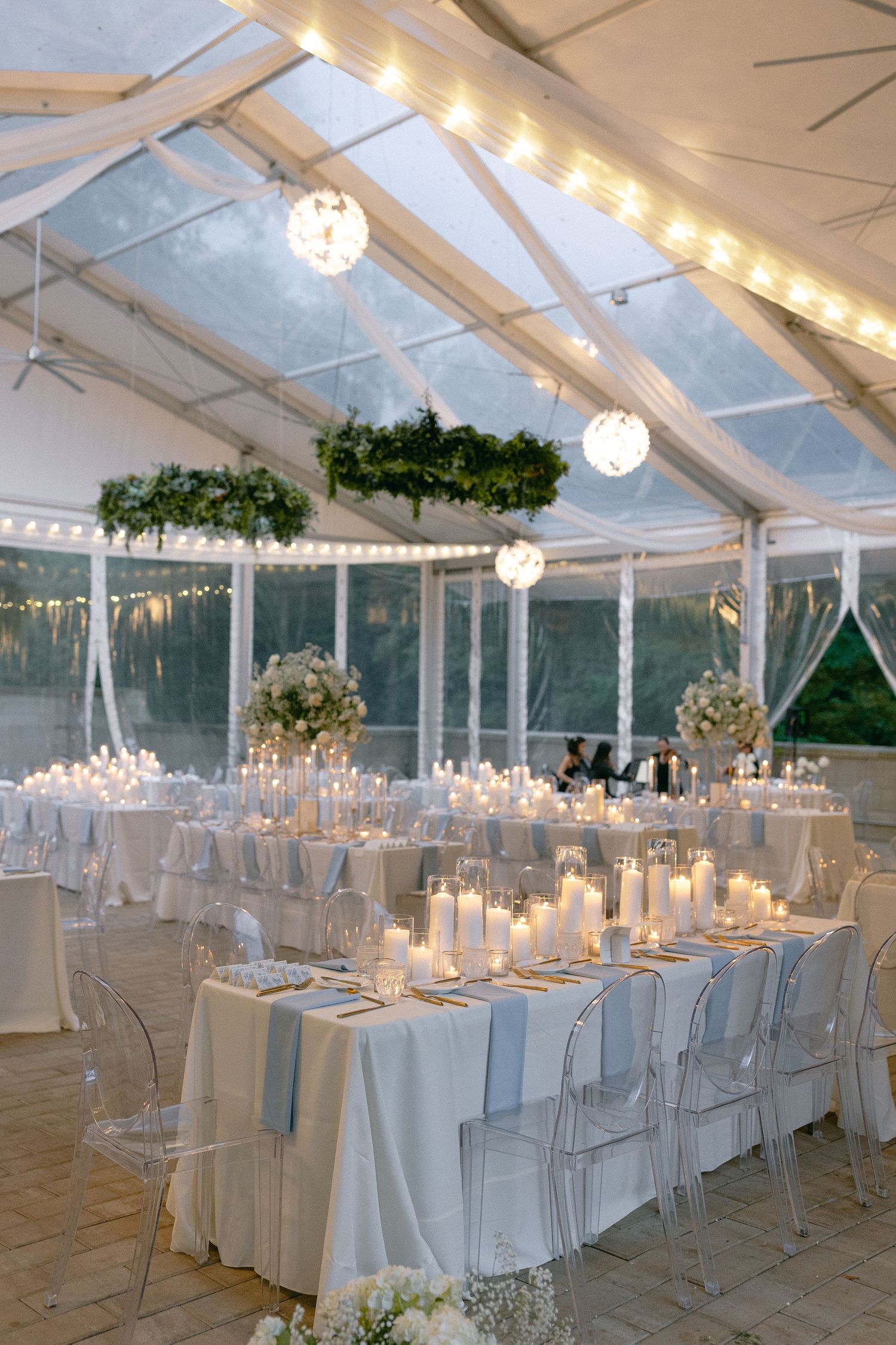 Elegant clear tent wedding reception with crystal chandeliers and white table settings.