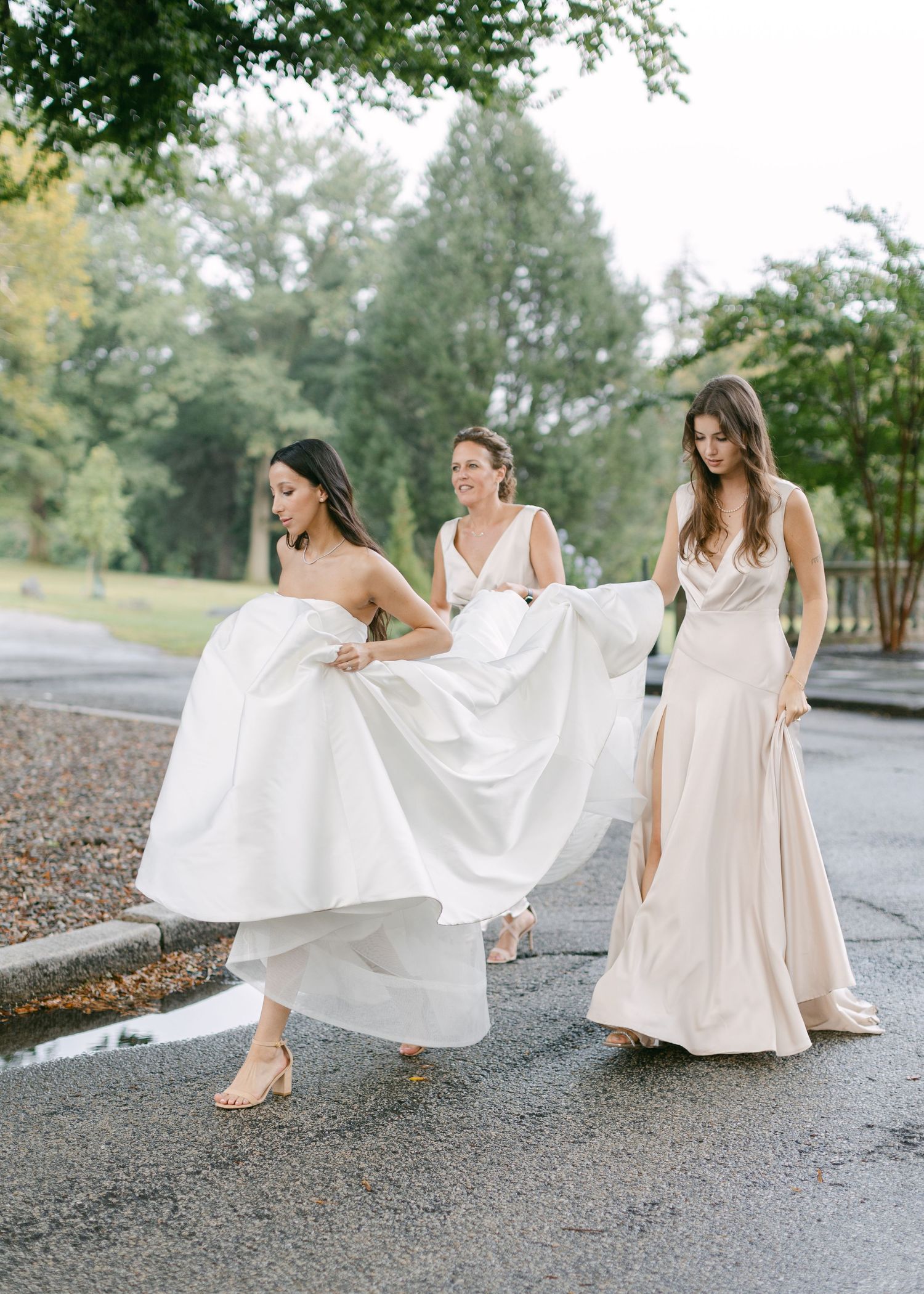 Bridesmaids in white and cream dresses twirling on a paved pathway.