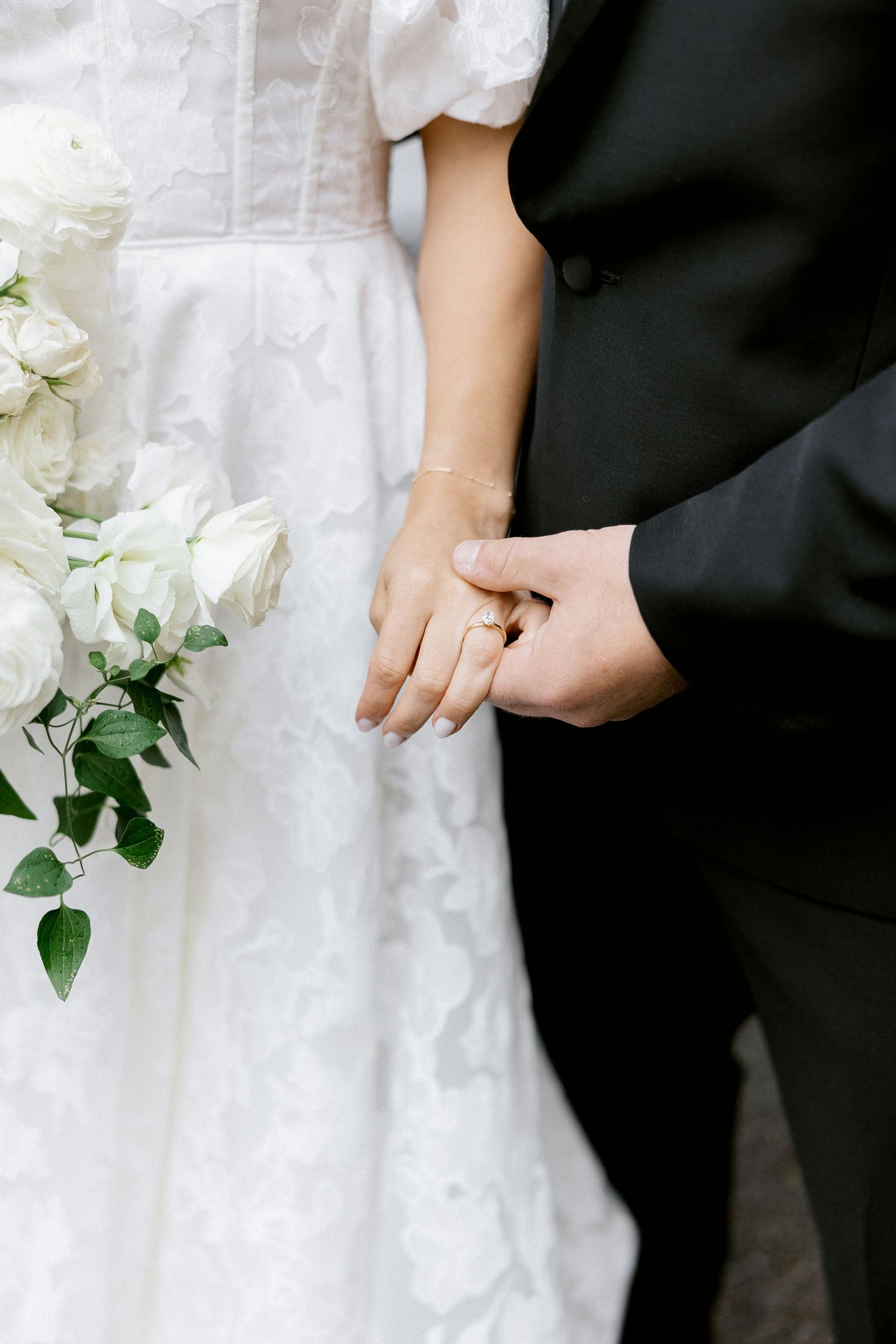 White wedding dress and black suit detail with white floral bouquet.
