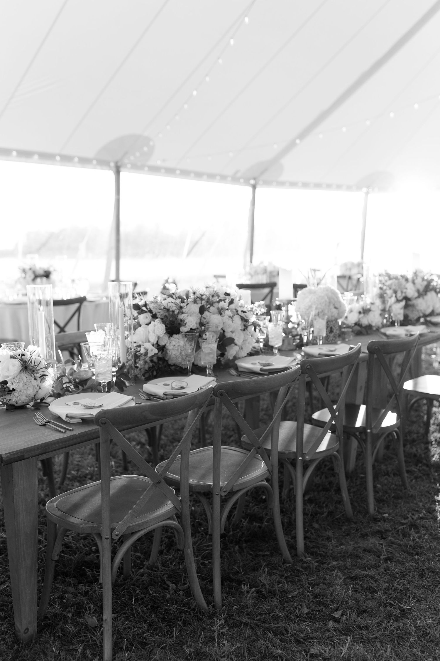 Wedding reception tent interior with cross-back chairs and floral centerpieces.