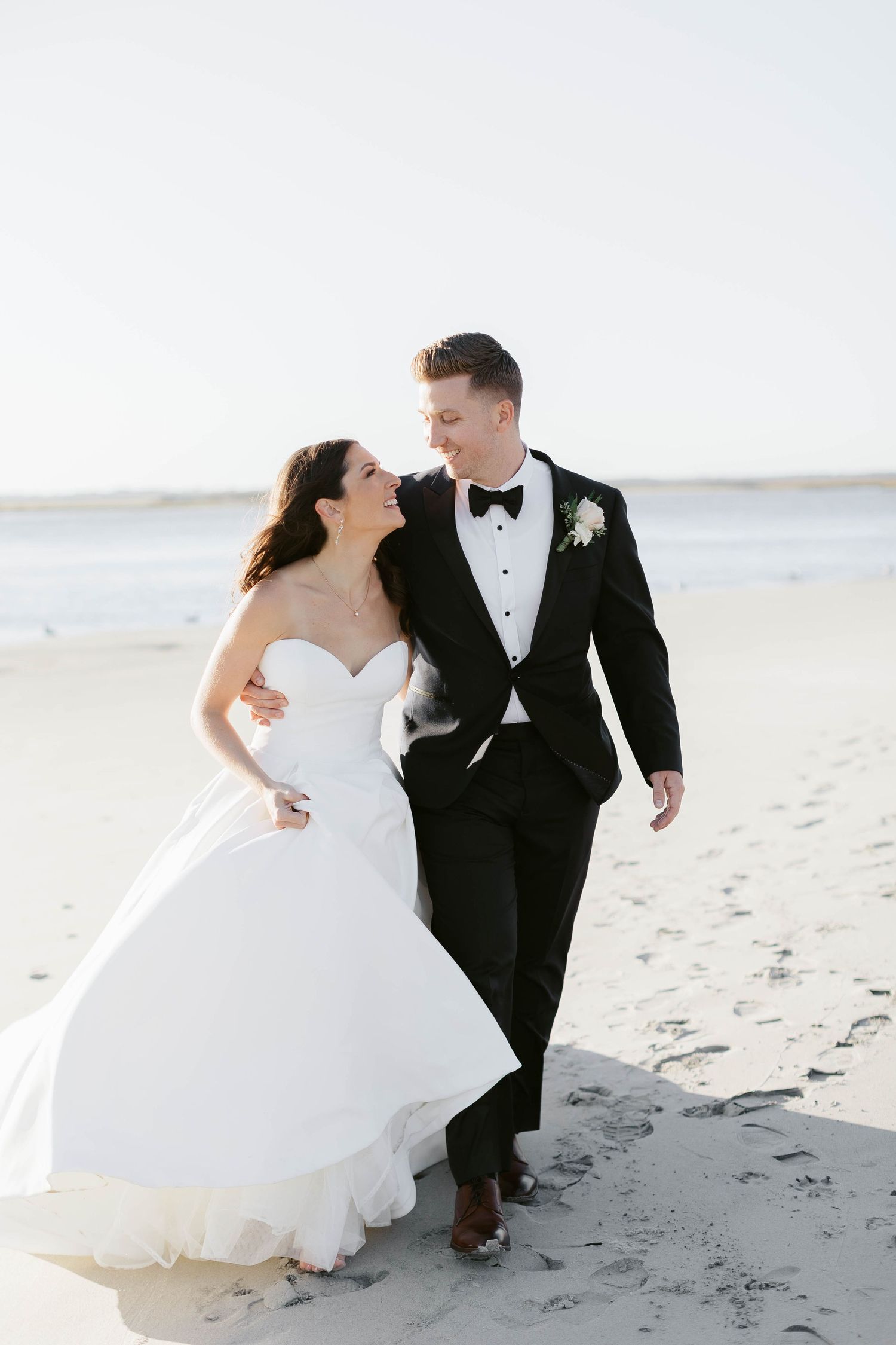 Joyful wedding couple shares intimate moments during beach photoshoot in classic black and white attire.