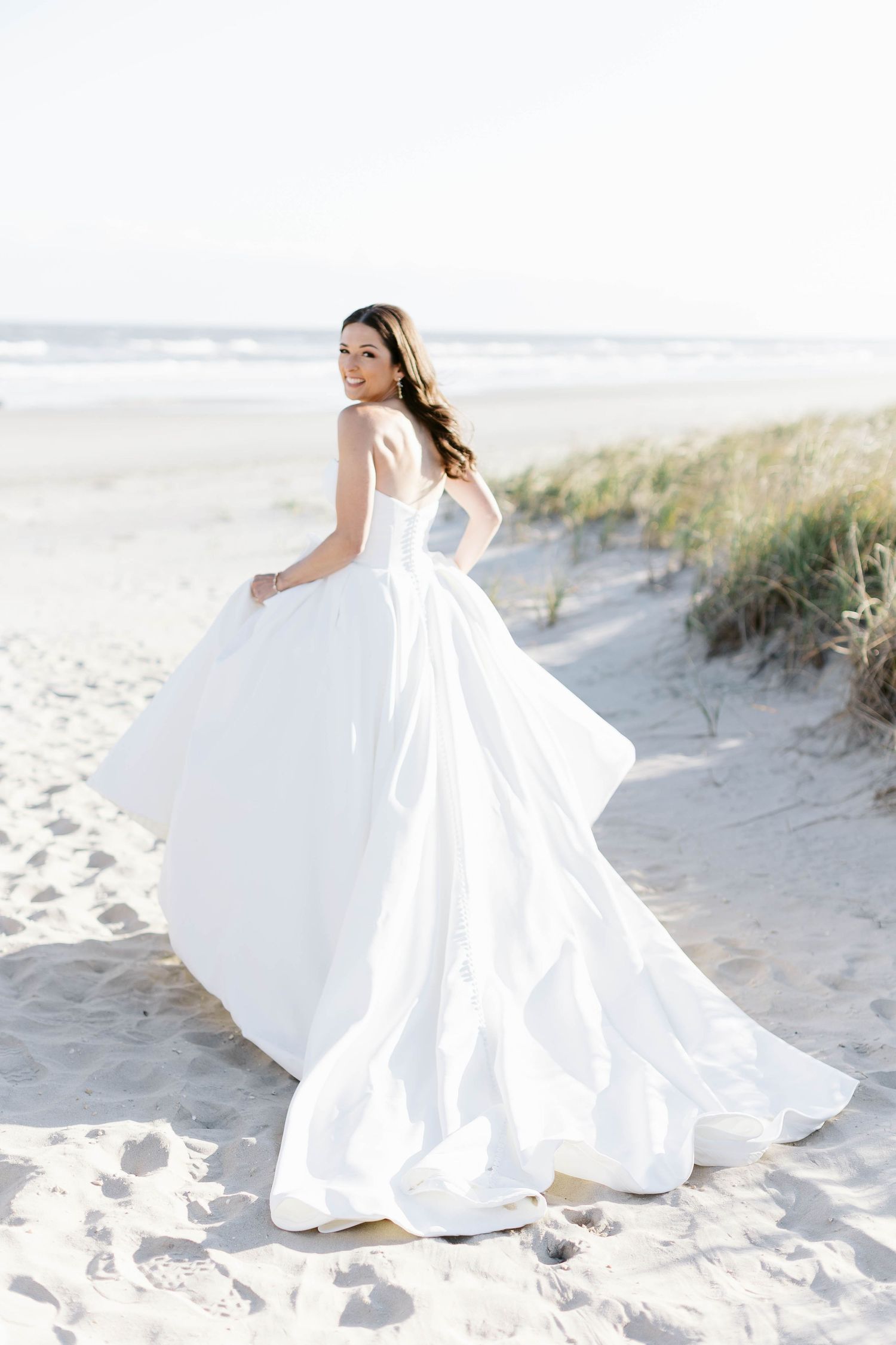 Ethereal bridal portraits show flowing white gown twirling on bright sandy beach.