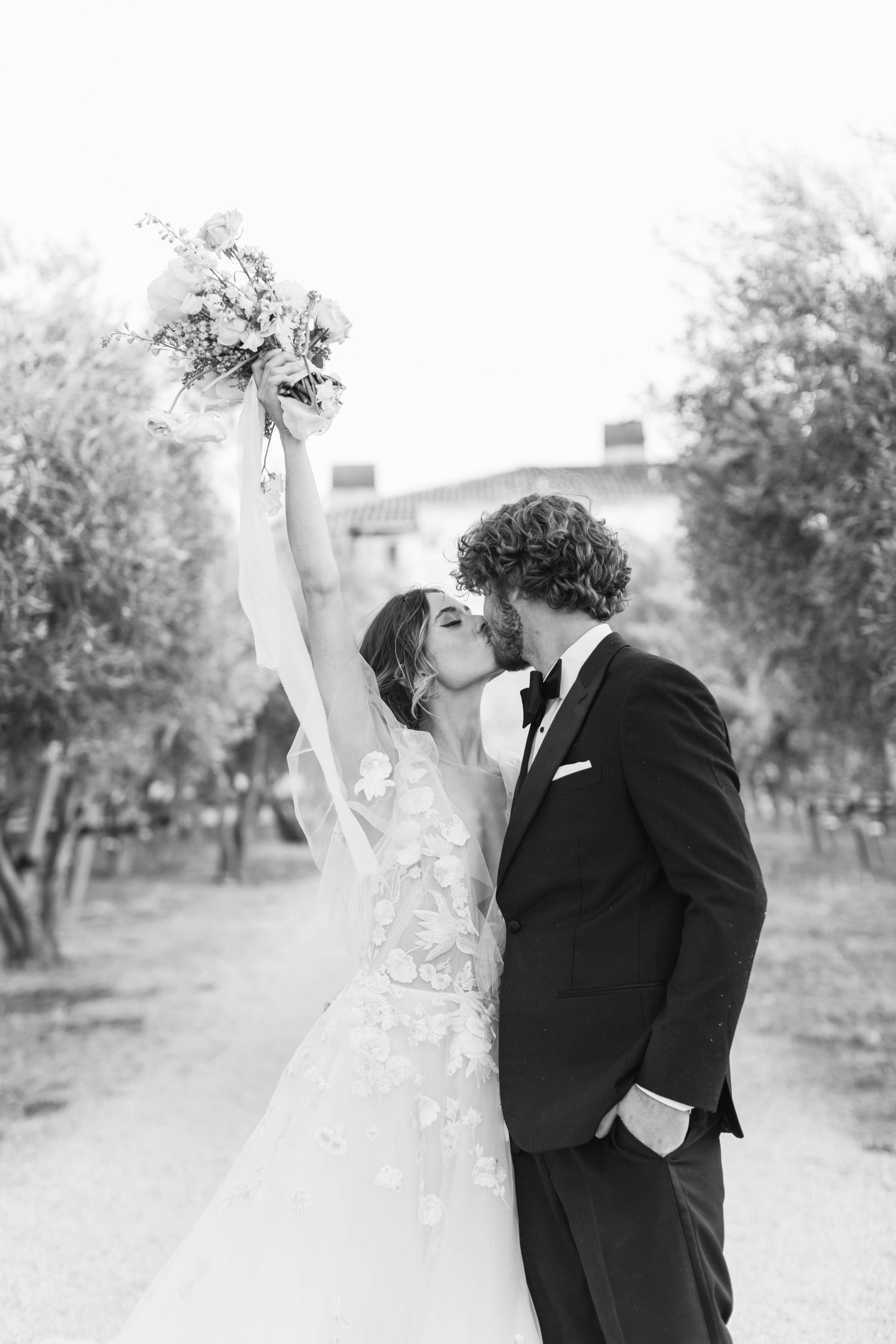 Romantic wedding couple embraces in an olive grove with soft natural lighting.