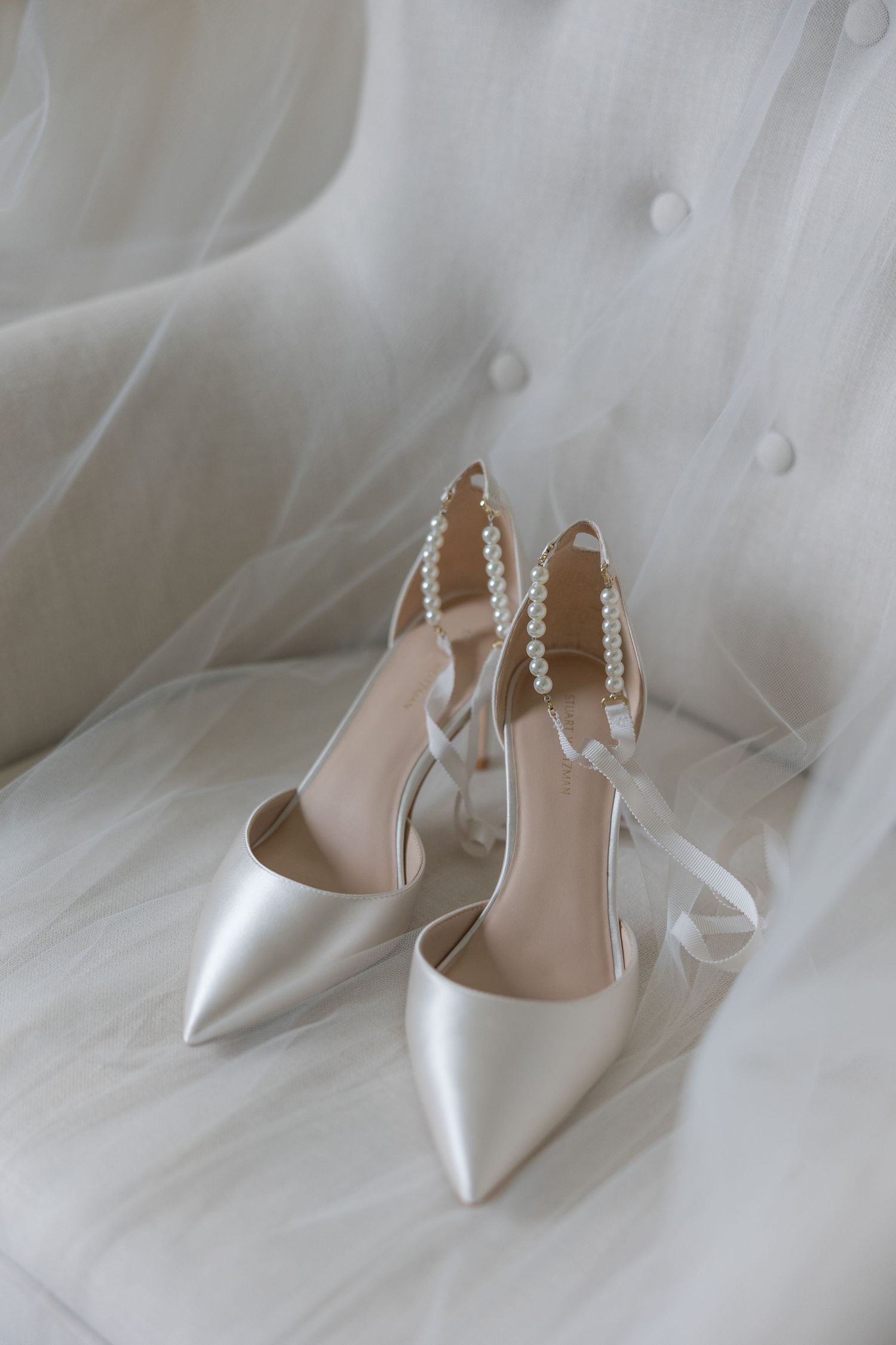 Elegant white satin Anne Klein bridal heels with pearl ankle straps displayed on white tulle fabric philadelphia wedding photographer