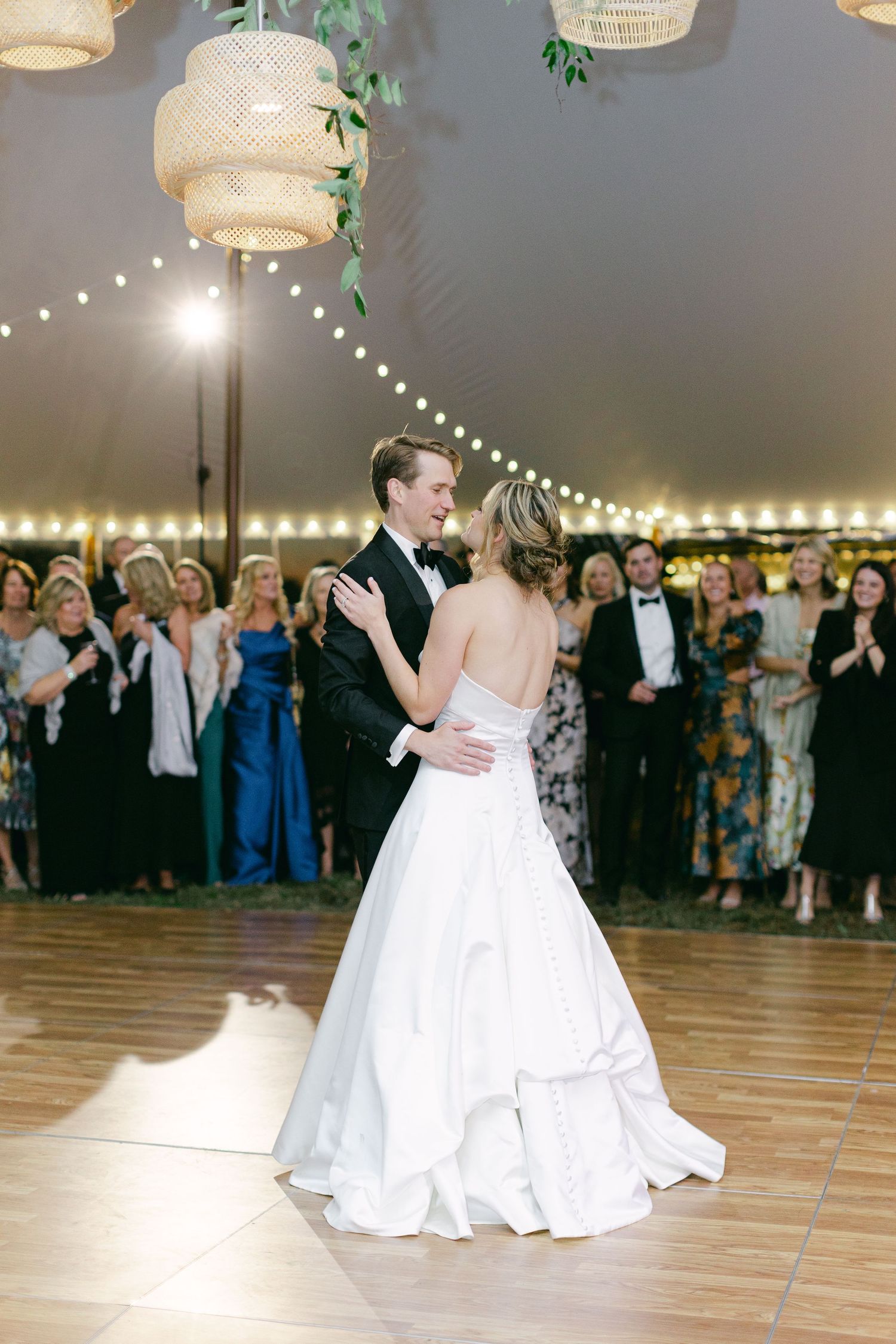 A couple shares their first dance under string lights at an elegant wedding reception.