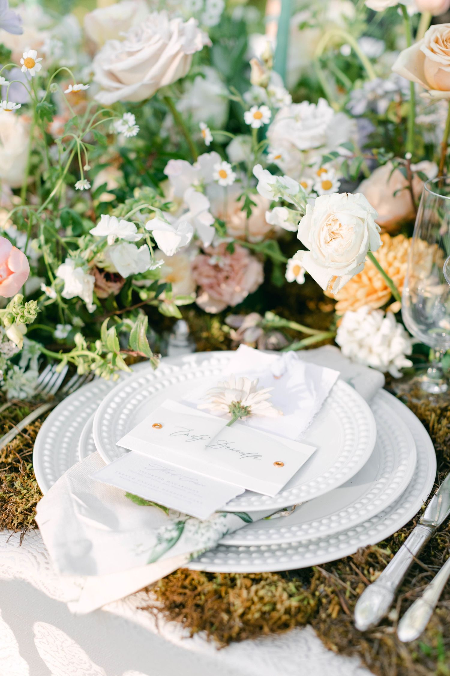 Elegant place settings with white plates and floral decorations for an outdoor wedding reception.