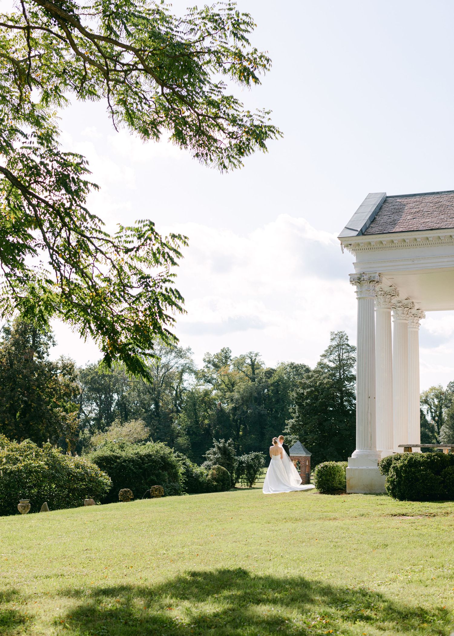 A scenic wedding venue with white columns and lush green landscaping on a grassy hillside.