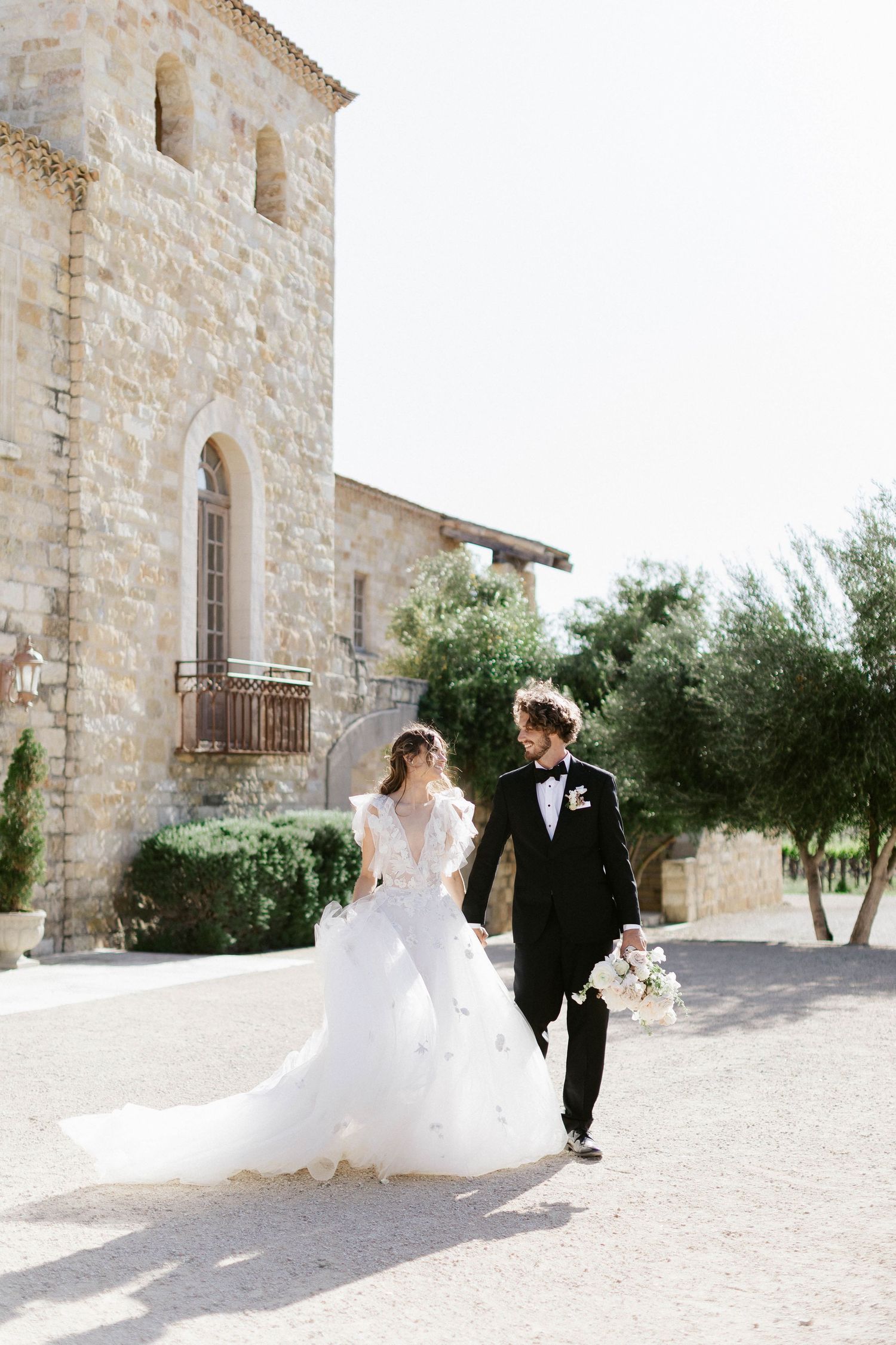 Wedding couple walks hand in hand along stone pathway at Mediterranean villa.