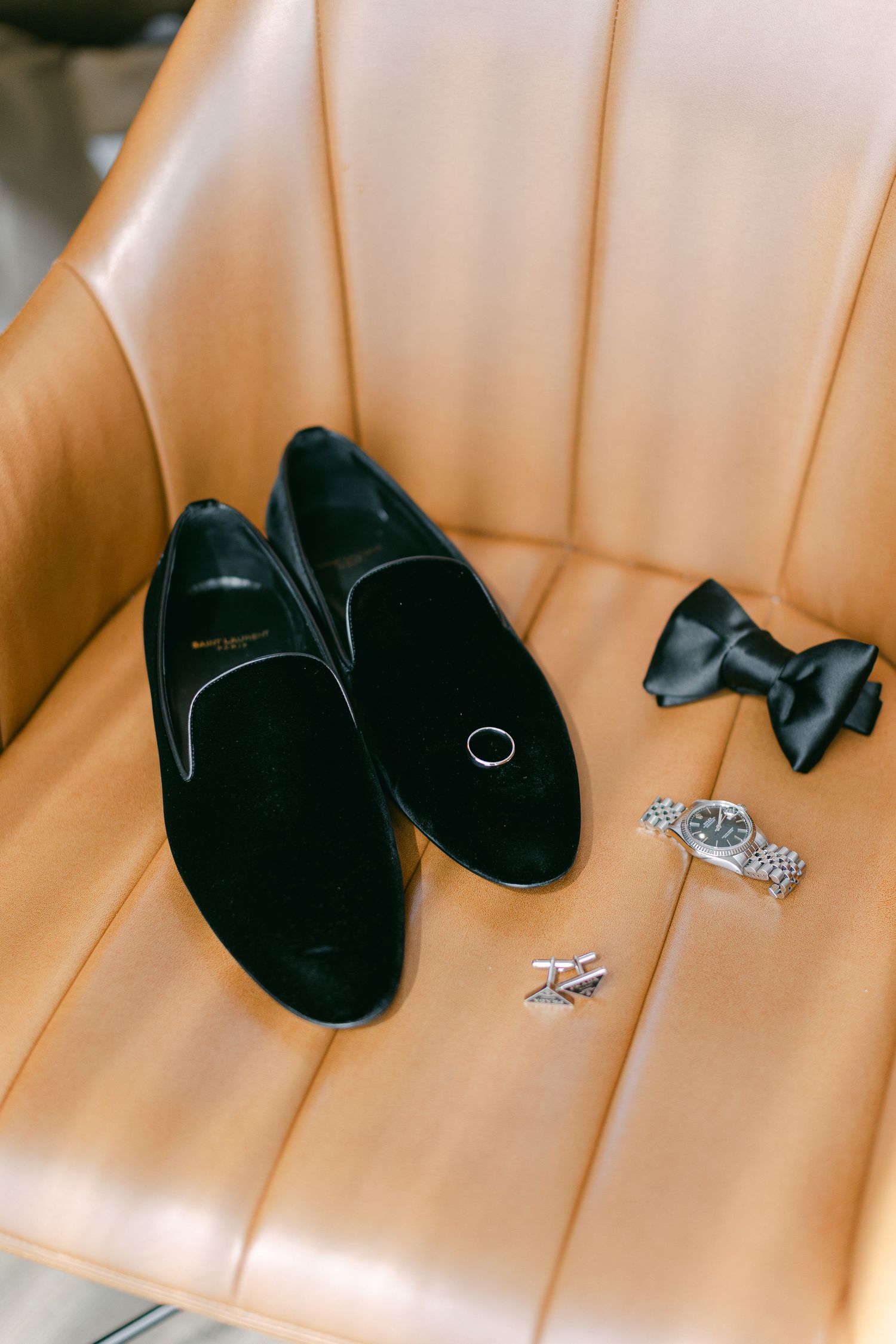 Wedding accessories including black velvet slippers and diamond rings on peach-colored seating.