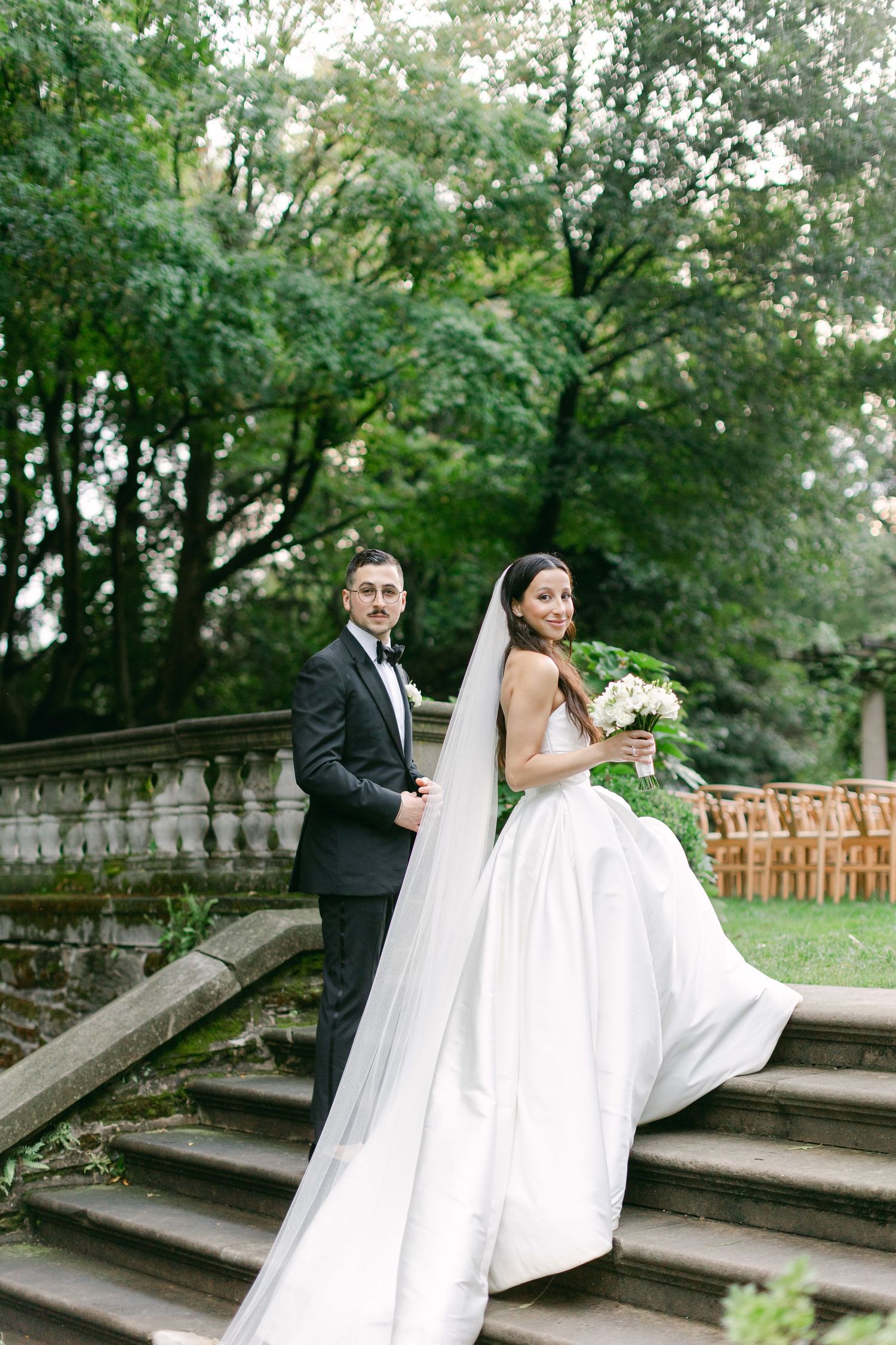 Wedding couple walking and posing on stone steps in an outdoor garden setting.