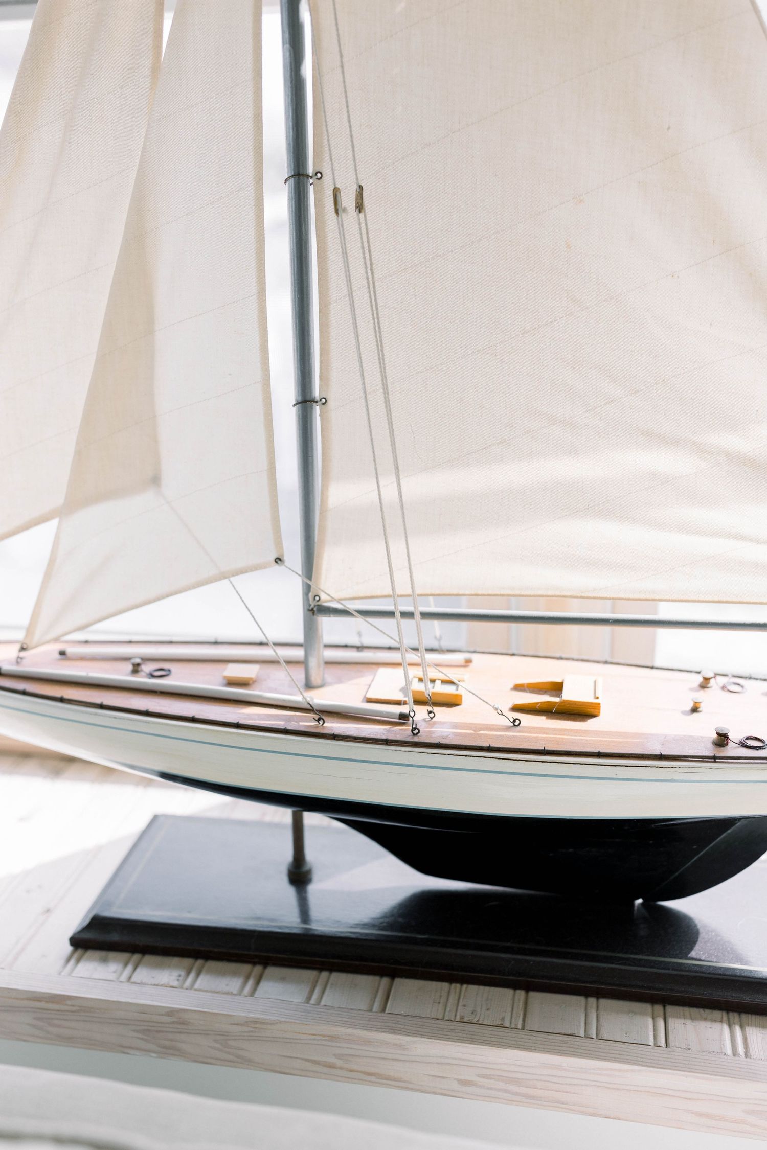 Model sailboat with white sails displayed on a wooden surface in natural light.