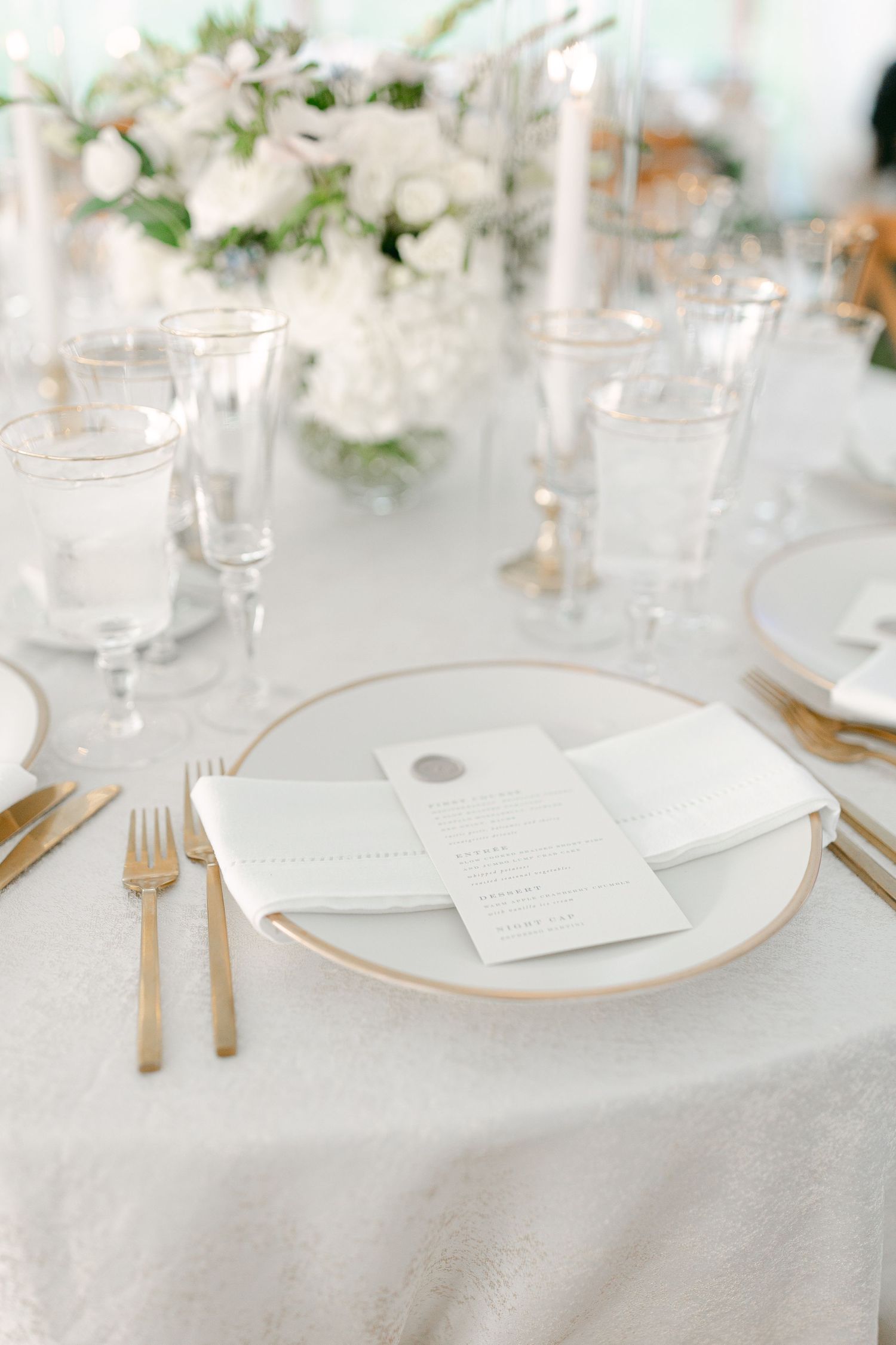 Elegant white table setting with gold flatware and delicate floral centerpieces at a wedding reception.