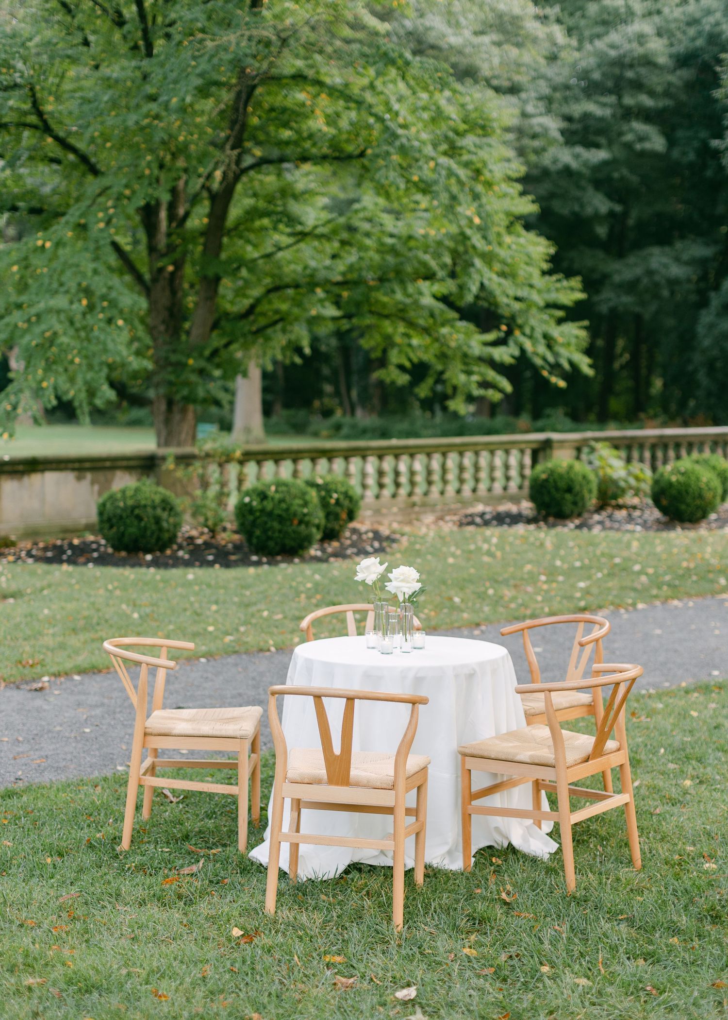 Outdoor wedding reception setup with wooden chairs and white tablecloths on a grassy lawn.