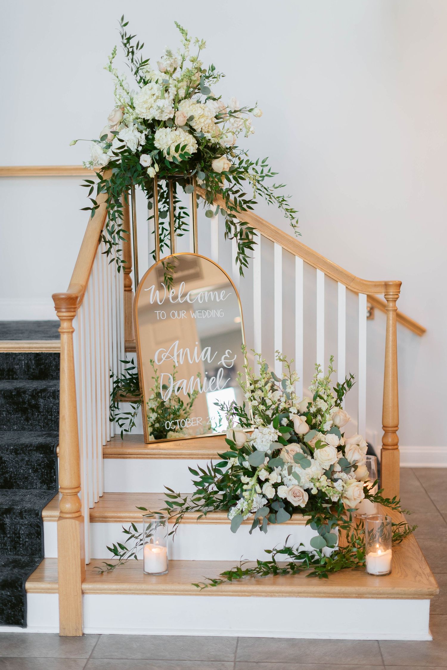 Elegant staircase decorated with white floral arrangements and welcome sign for wedding ceremony.