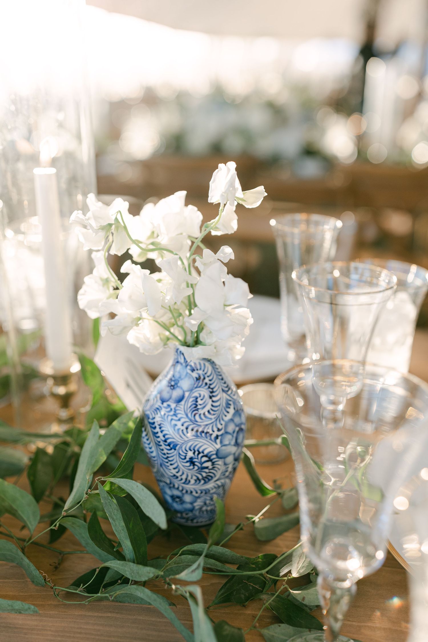 Elegant table setting with white flowers in a blue chinoiserie vase and crystal glasses.