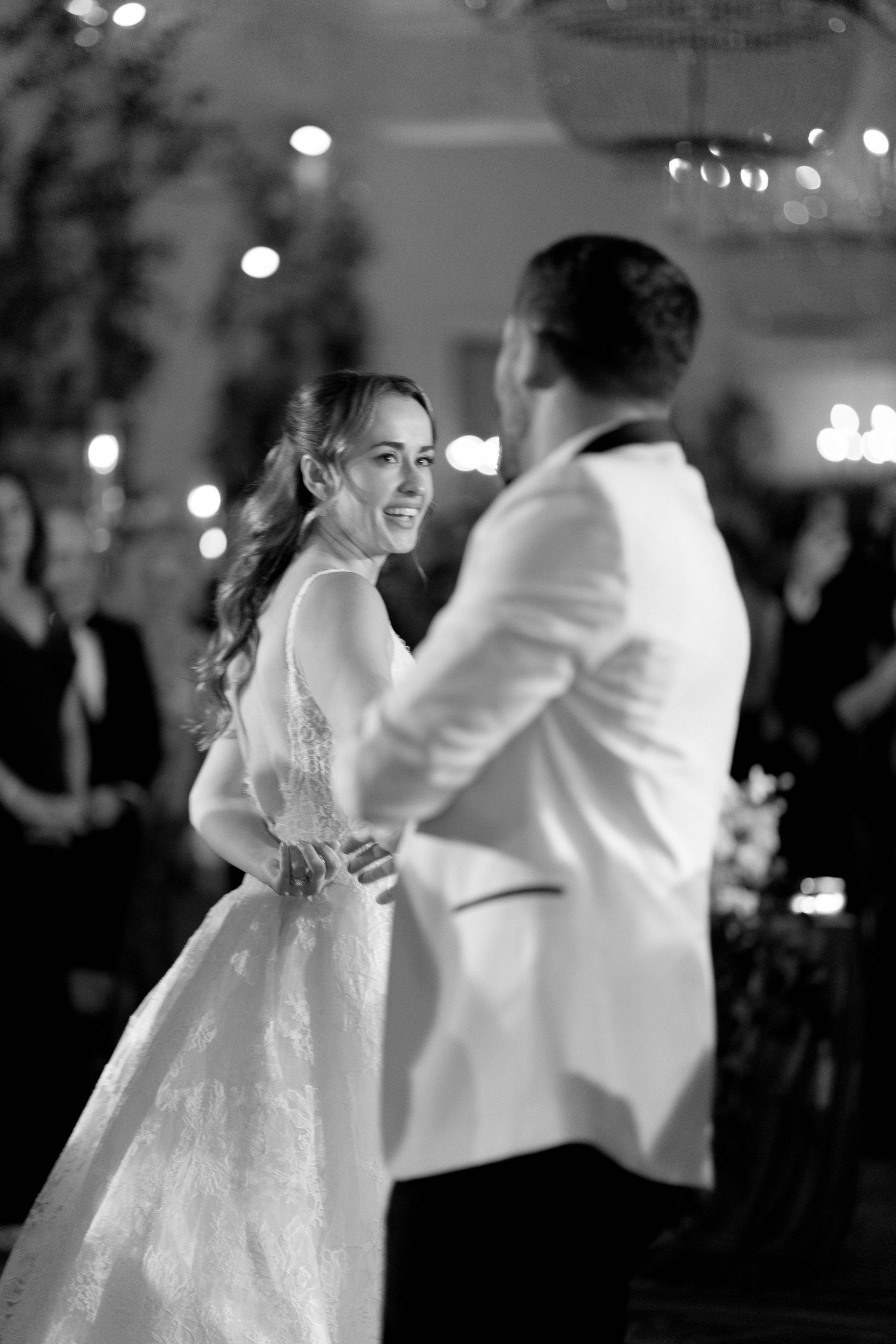 A bride and groom share their first dance at a wedding reception with twinkling lights in the background.