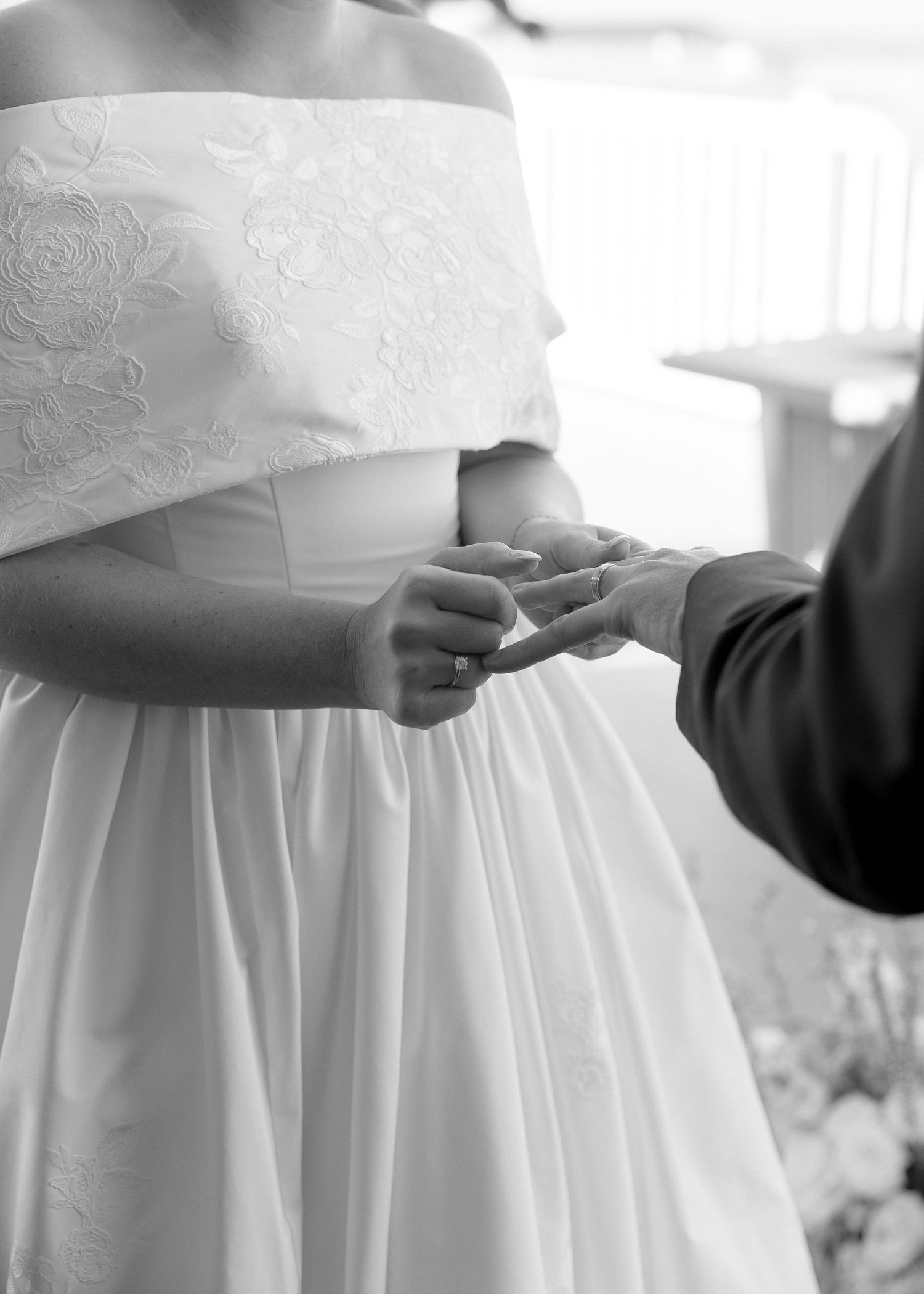 A close-up black and white photo of a ring exchange at a waterfront elegant wedding