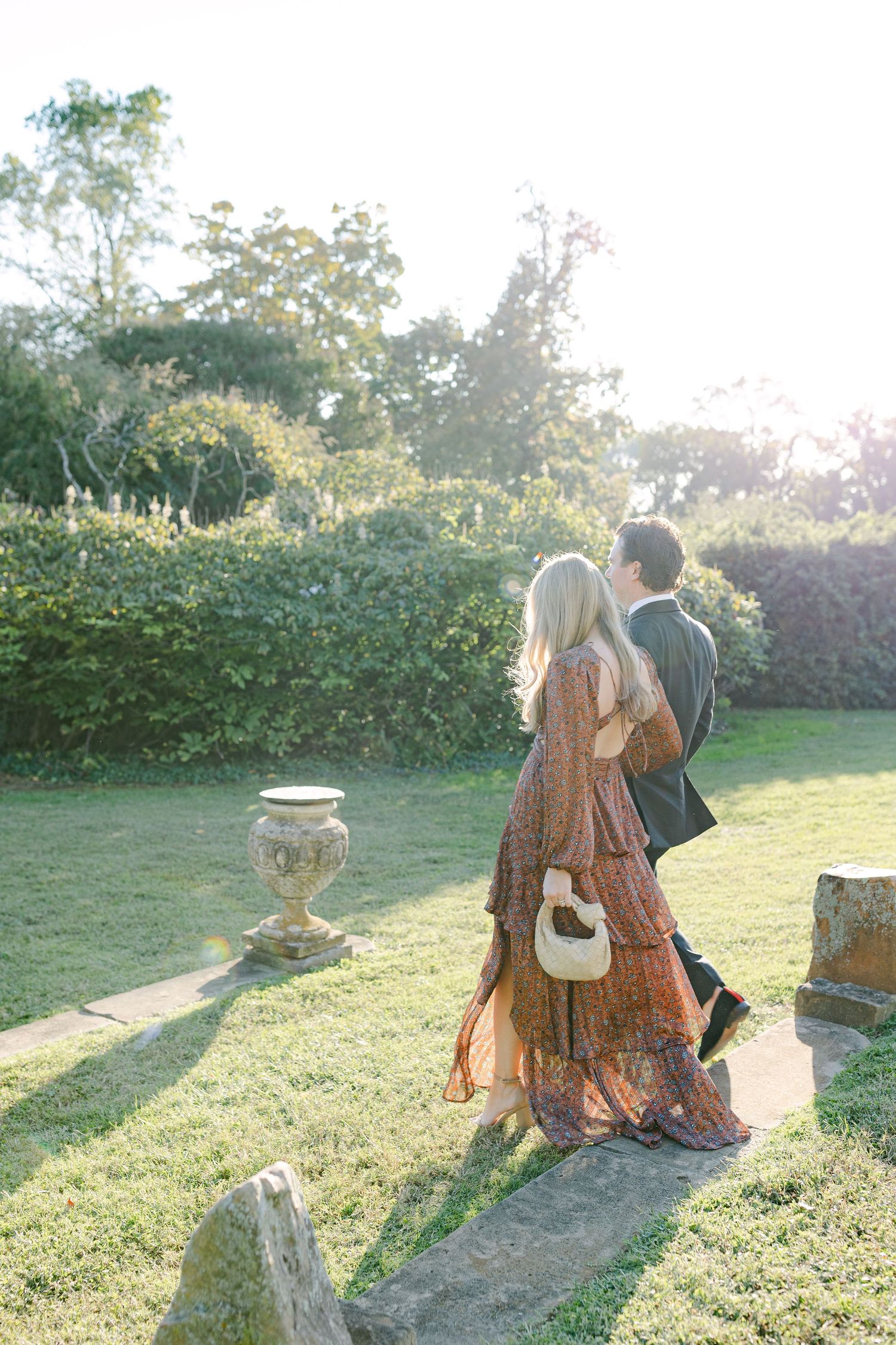 Wedding couple relaxes on rustic wooden stumps in a garden setting at sunset.