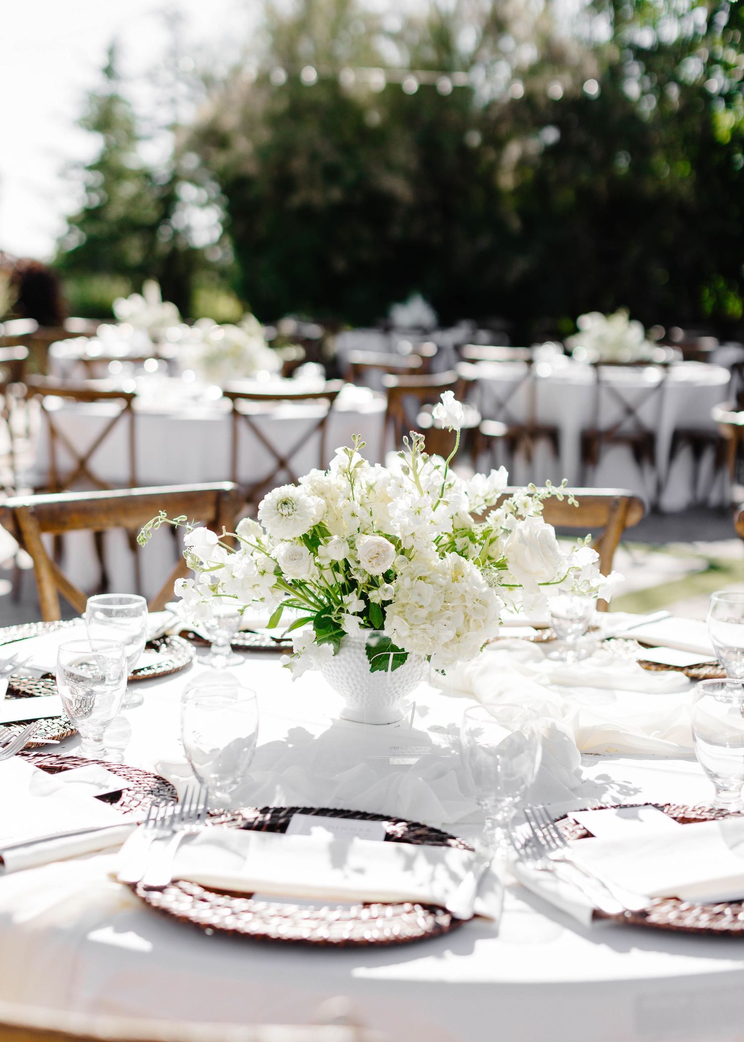Elegant wedding reception table settings with white floral centerpieces and rustic wooden chairs.