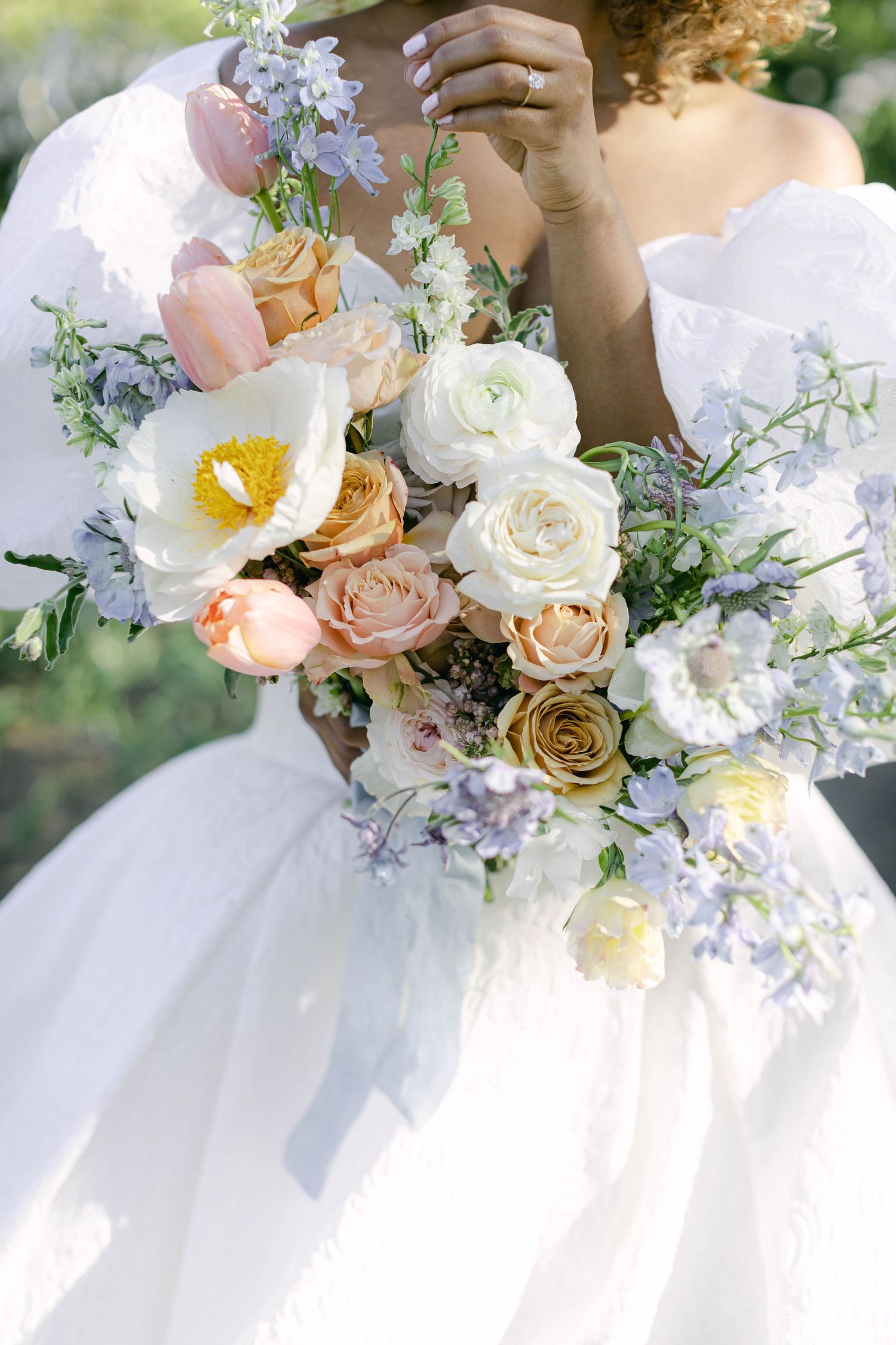 A delicate wedding bouquet features peach roses, white orchids, and soft purple blooms against a white dress.