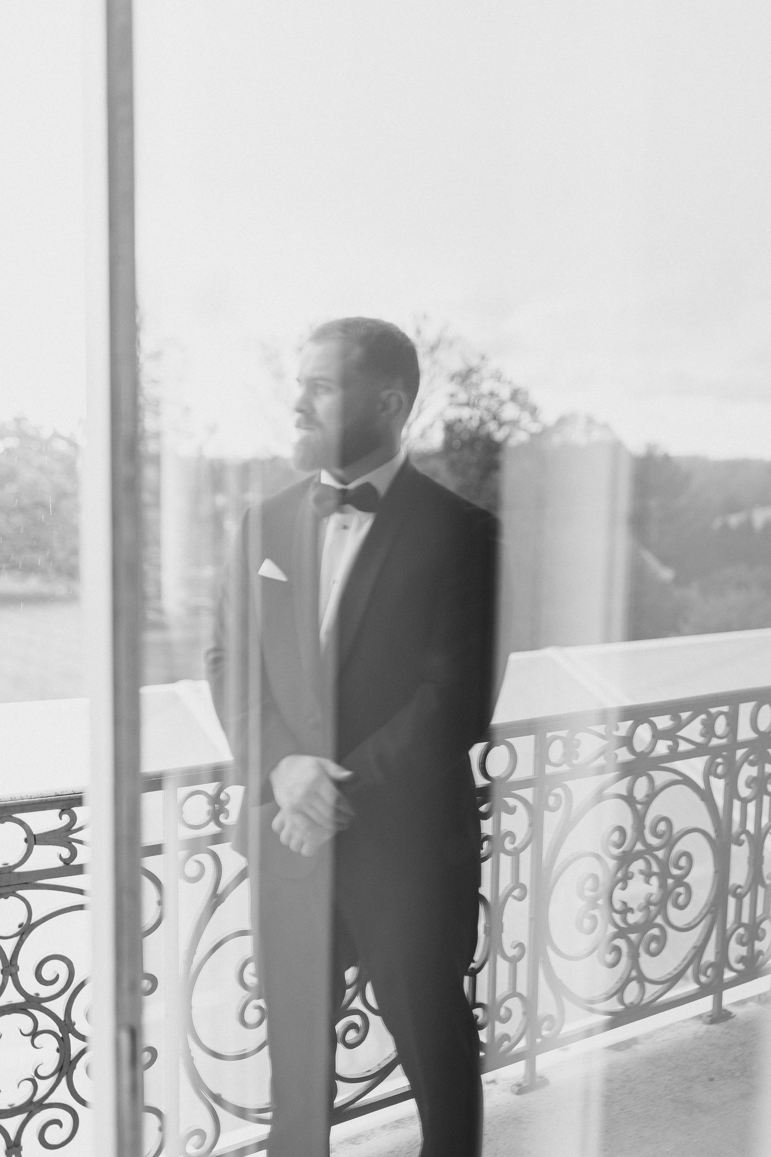 A black and white portrait of a groom in tuxedo standing by decorative railings.
