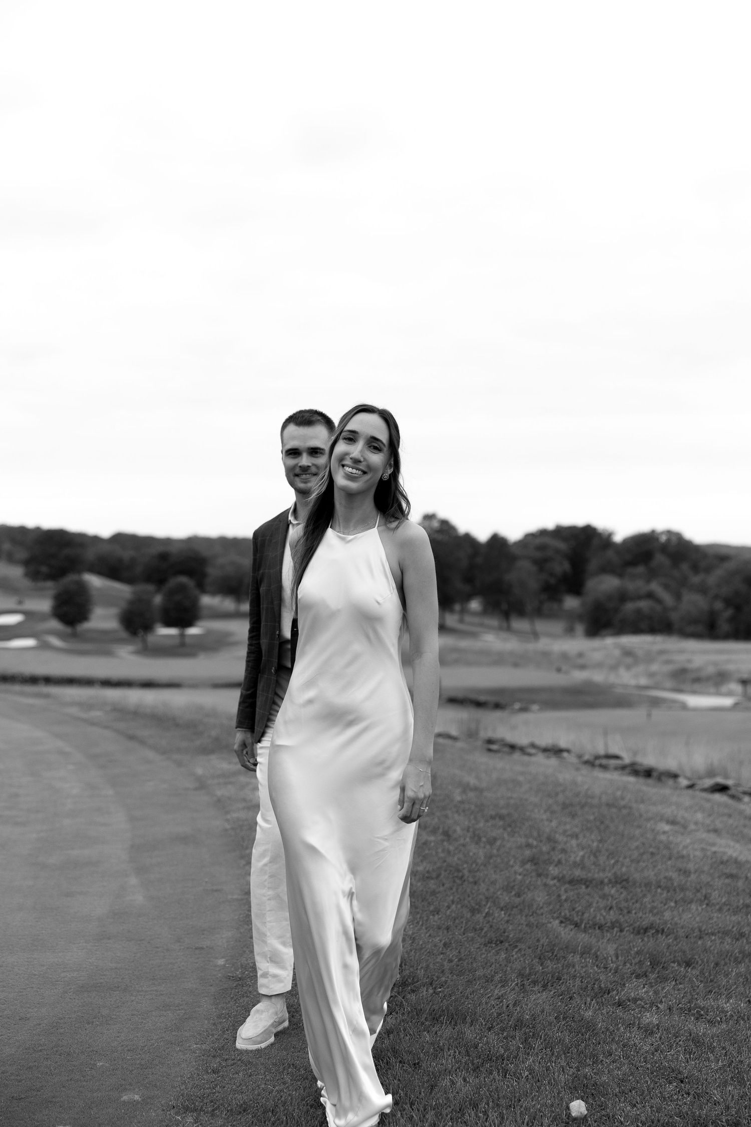 Black and white portrait of a couple standing on a golf course landscape during their rehearsal dinner the night before their wedding day.