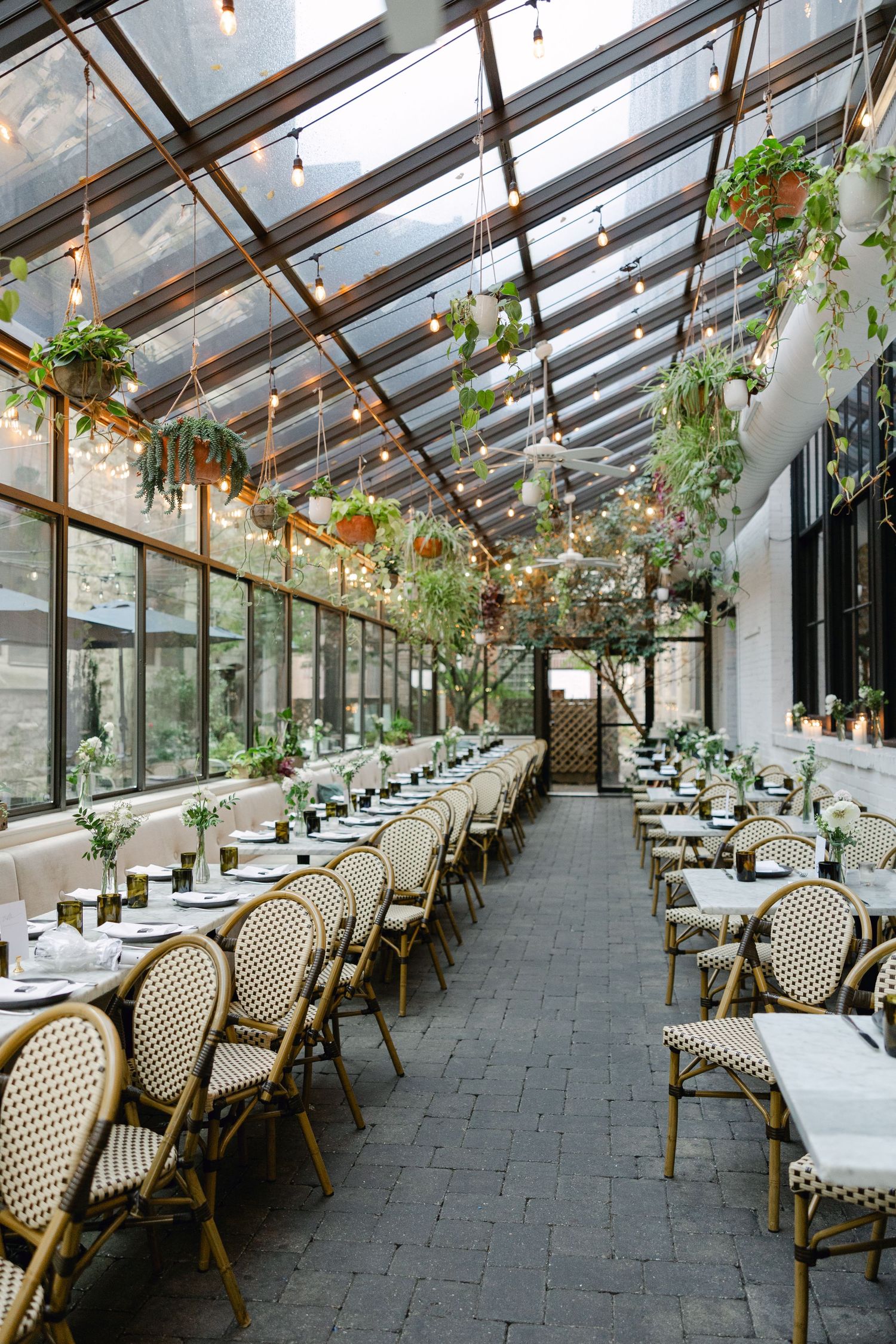 An elegant greenhouse wedding reception venue with glass ceiling, hanging plants and bistro chairs.