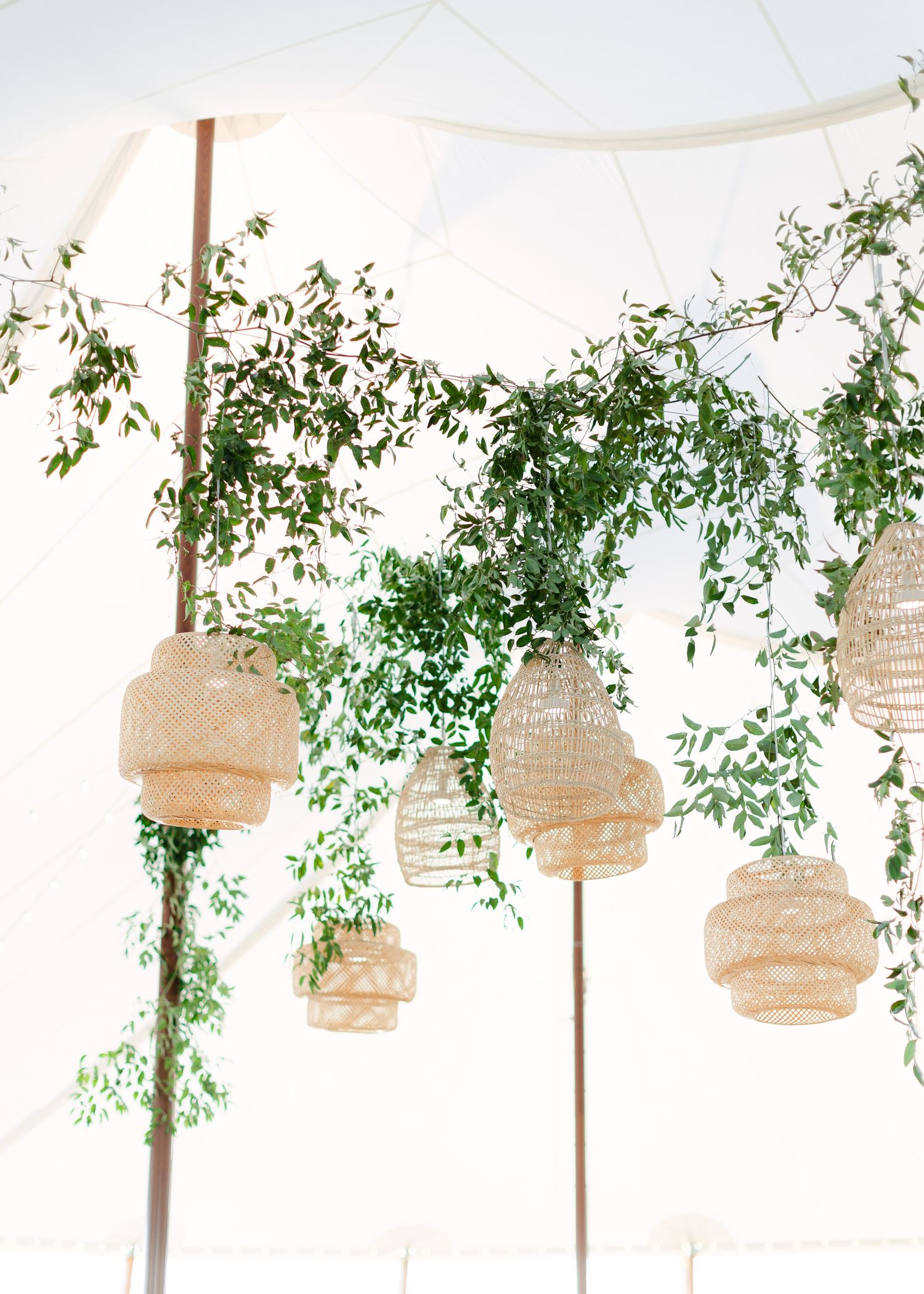 Natural woven pendant lights hang from tent ceiling with cascading greenery.