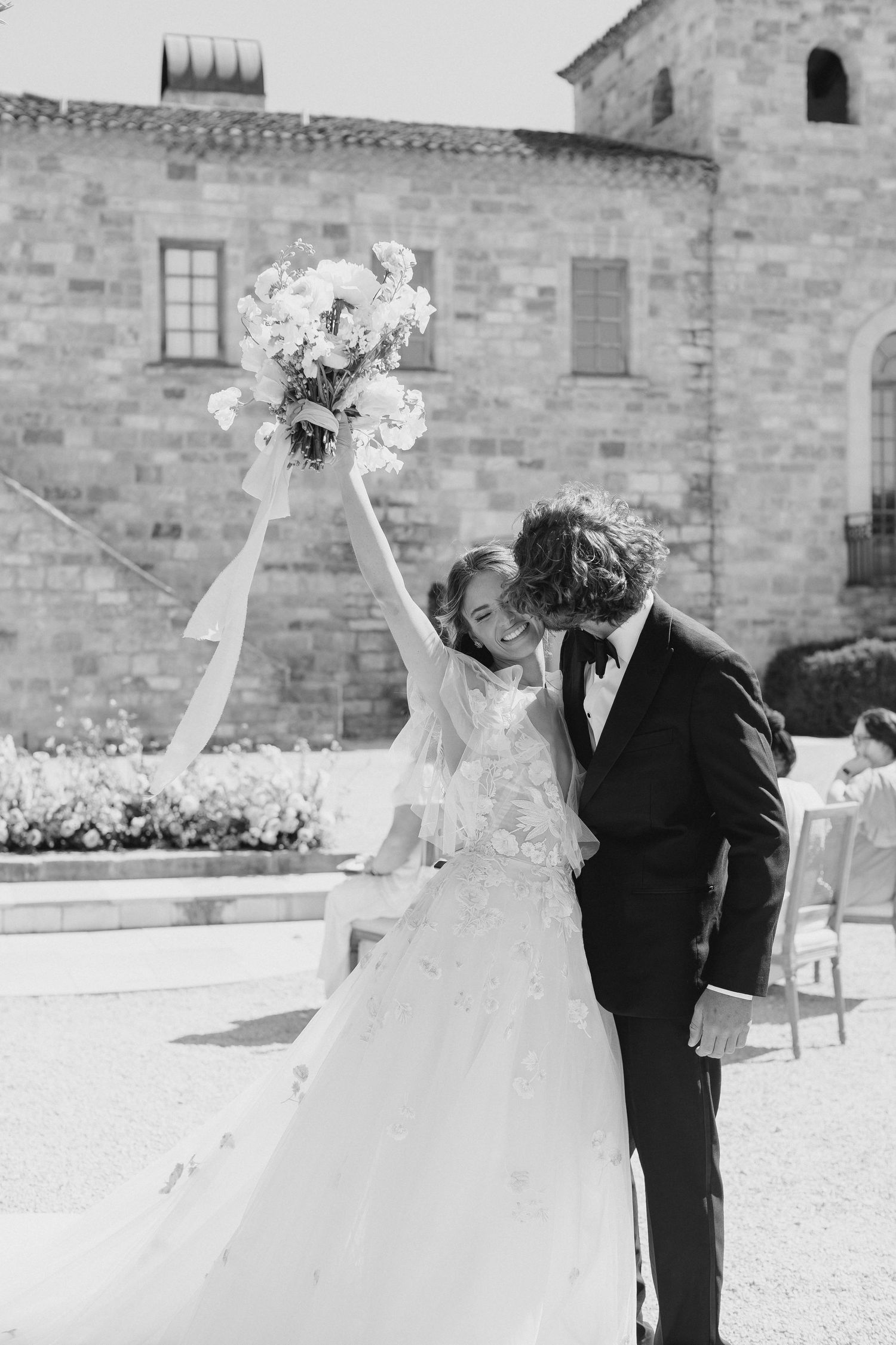 Newlyweds share intimate moment against historic stone building backdrop.