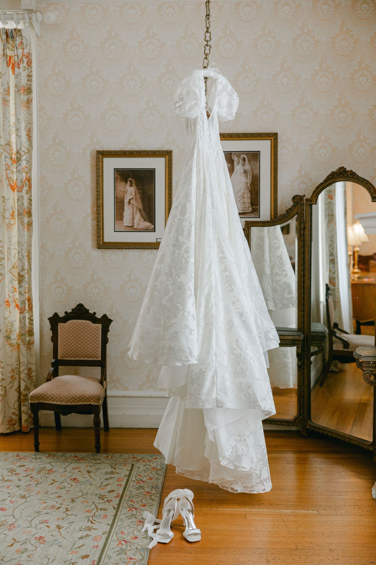 Elegant bridal preparation room with hanging white dress and vintage furniture.