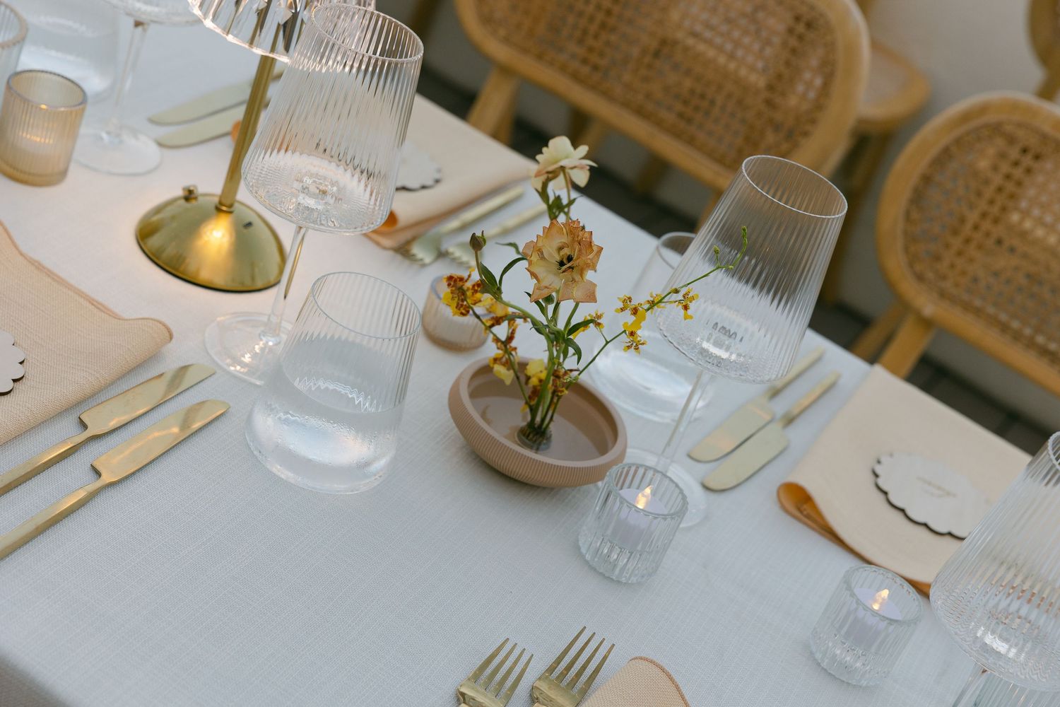 Elegant wedding table setting with rattan chairs and gold accents.