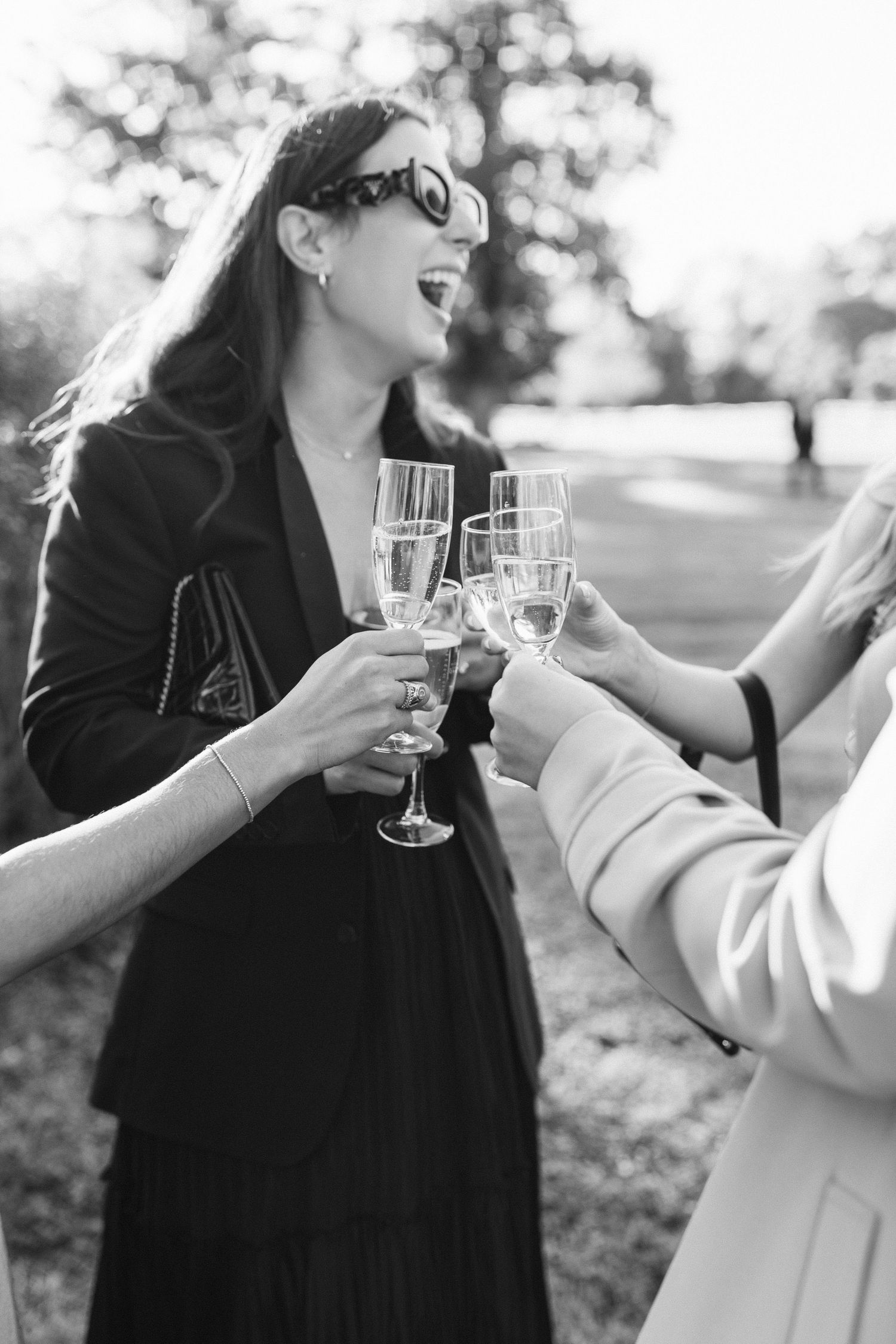 Candid moment of wedding guests toasting and laughing together during an outdoor celebration.