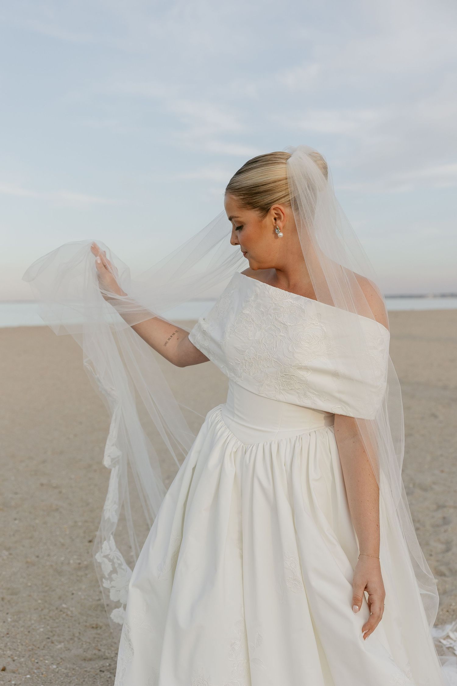 Elegant bride in a timeless dress and veil stands on a beach at the Lewes Yacht Club Vogue style true to color wedding photographer