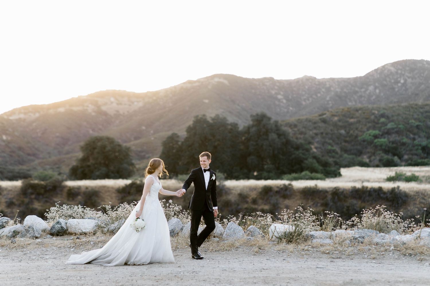 A romantic wedding couple poses against a mountainous desert landscape at sunset.