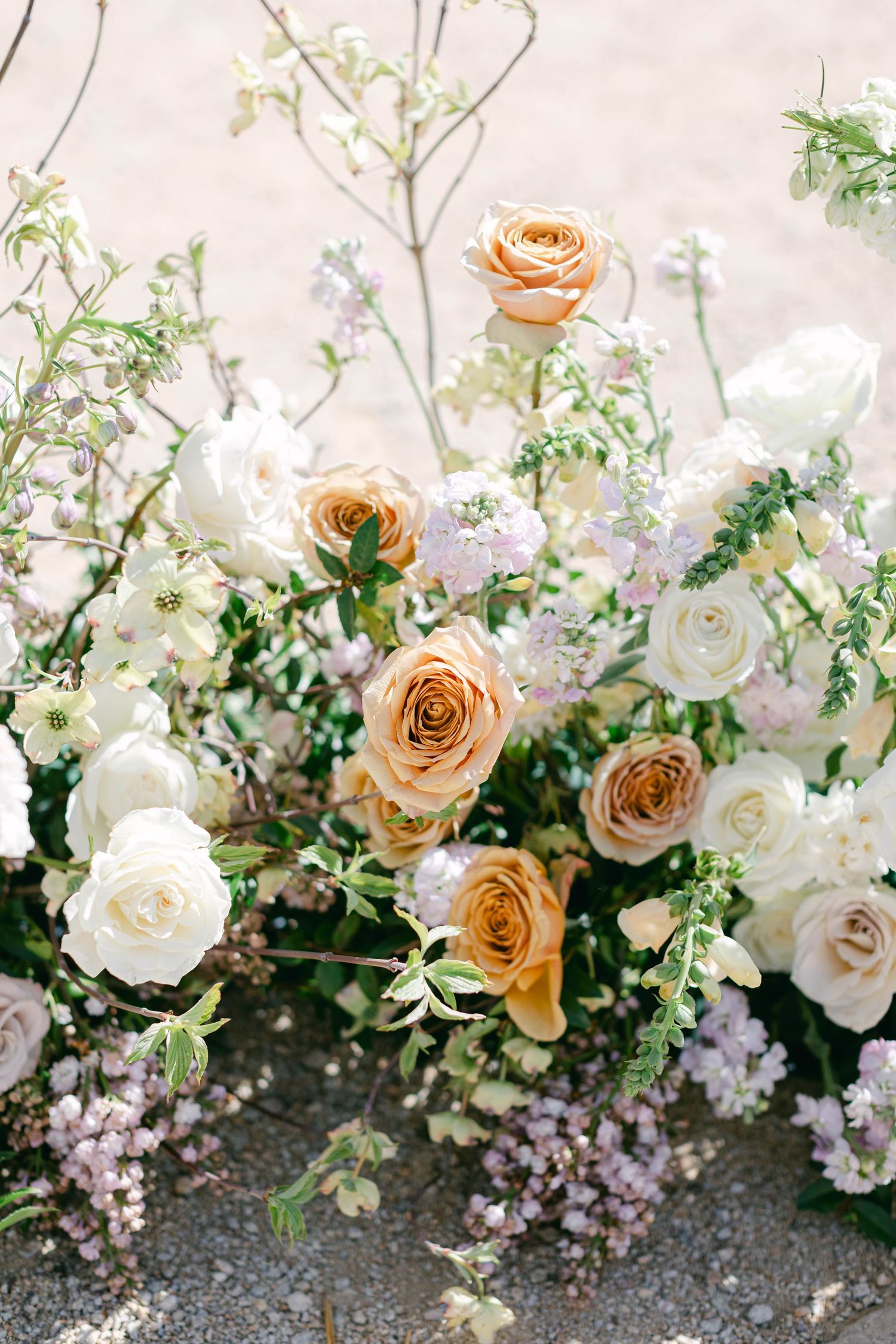 Romantic floral arrangement with peach and white roses cascading along stone pathway.