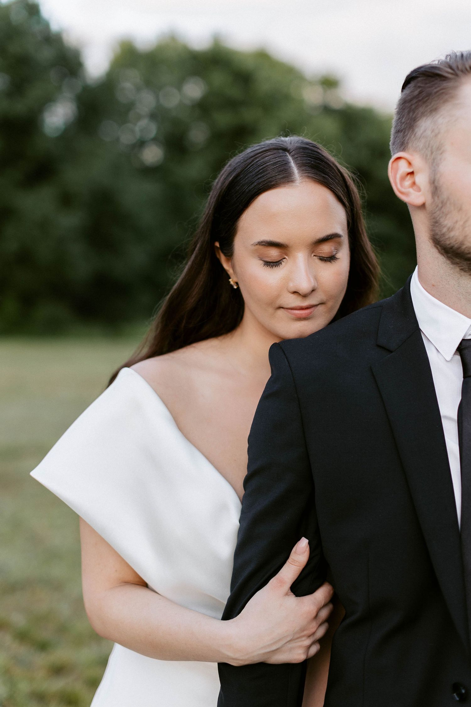 Intimate wedding portrait in an outdoor setting with classic black and white formal attire.