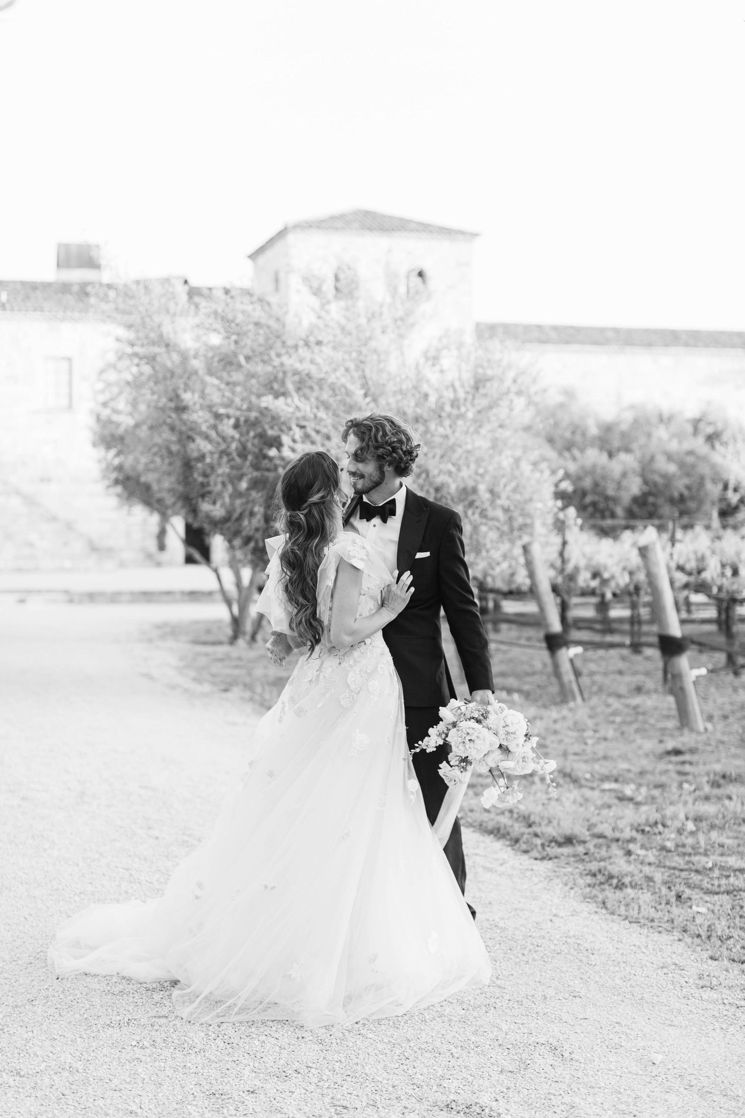 Black and white wedding portrait of couple embracing in an orchard.