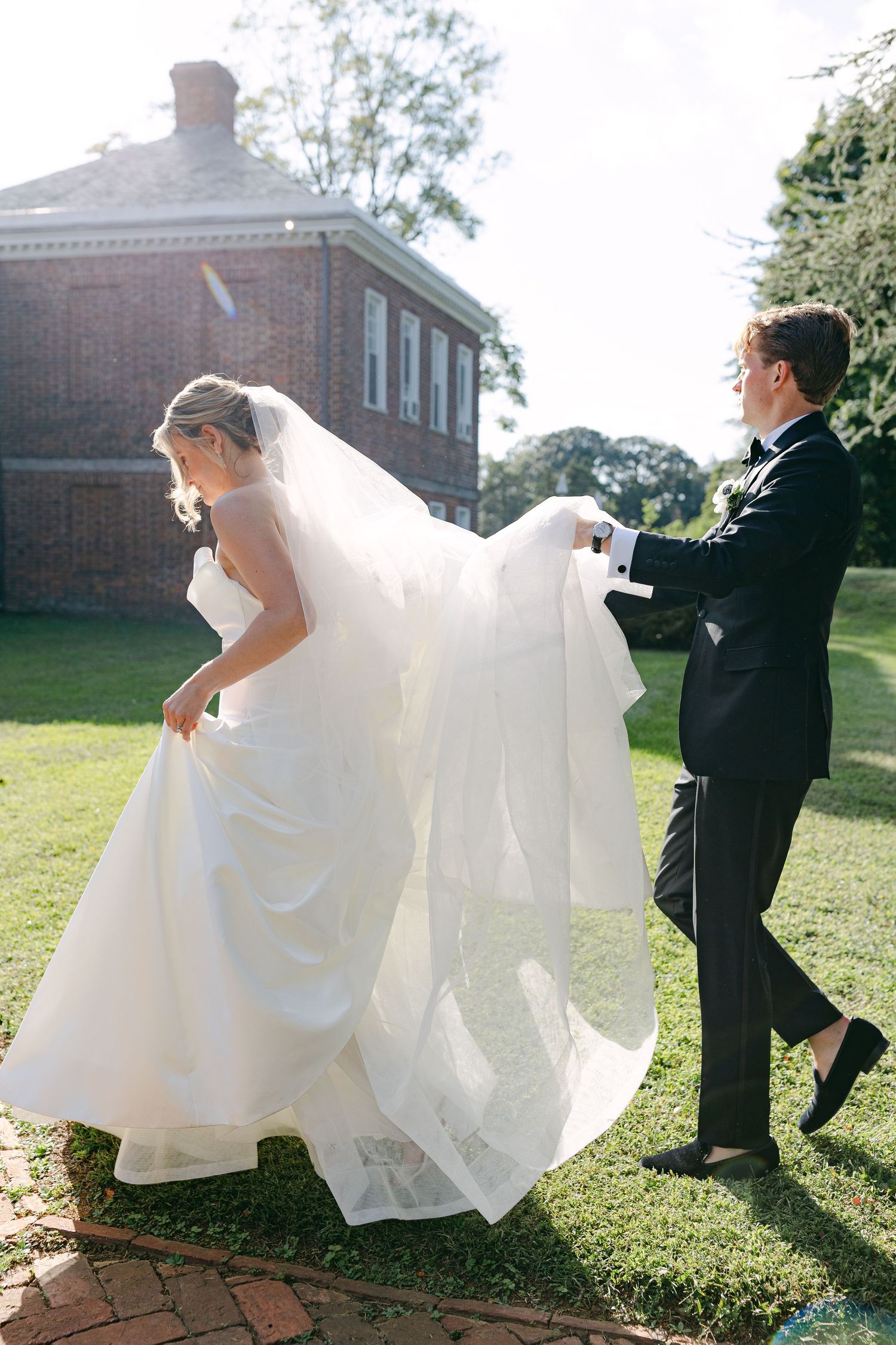 Wedding couple dances outdoors as bride's white dress flows dramatically in the sunlight.