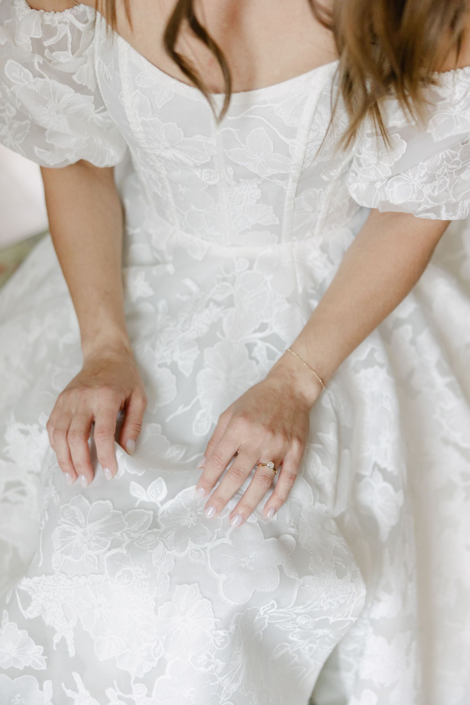 Close-up of hands smoothing white lace fabric on wedding dress.