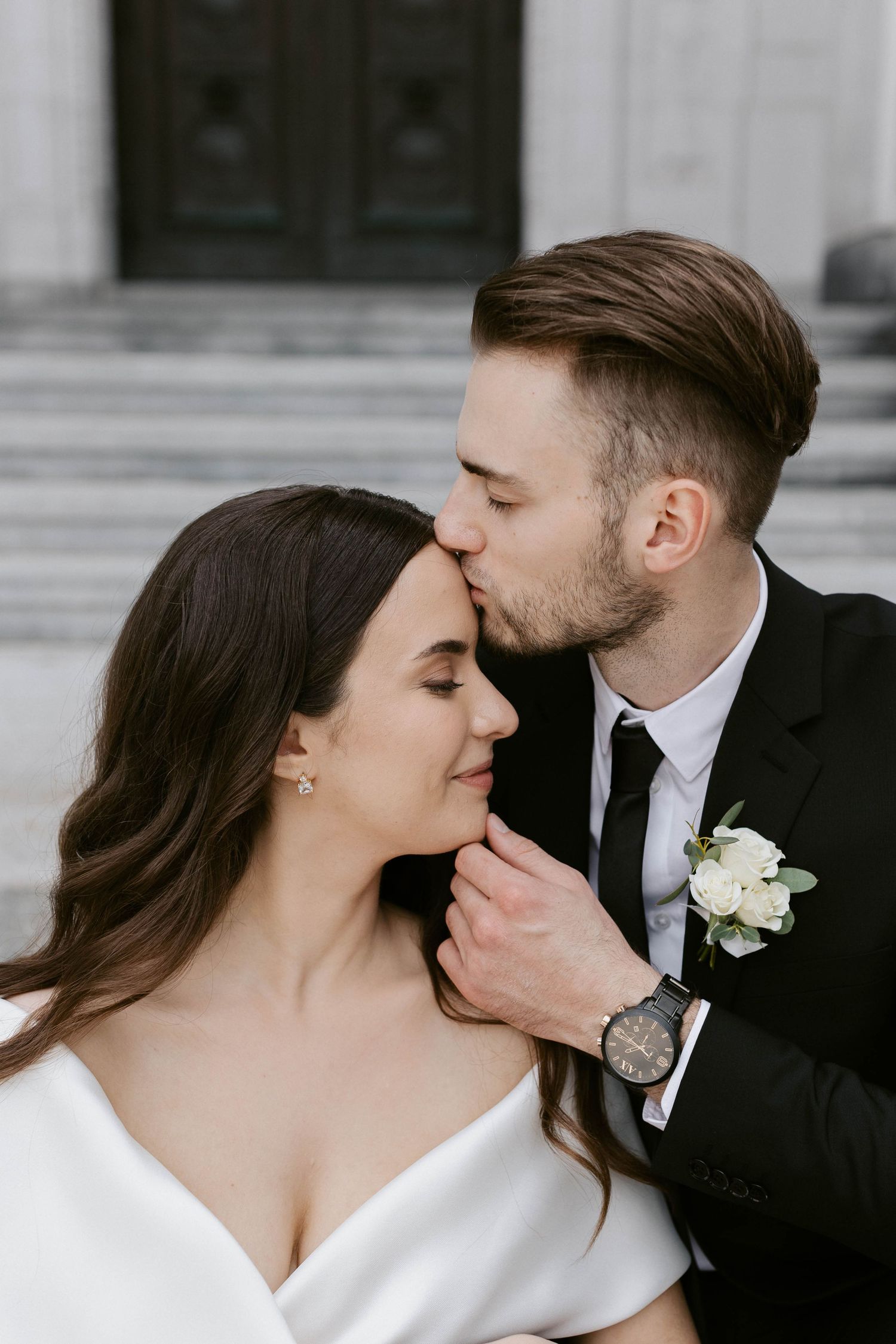 A romantic wedding portrait showing tender moments between newlyweds in formal attire against a classic backdrop.